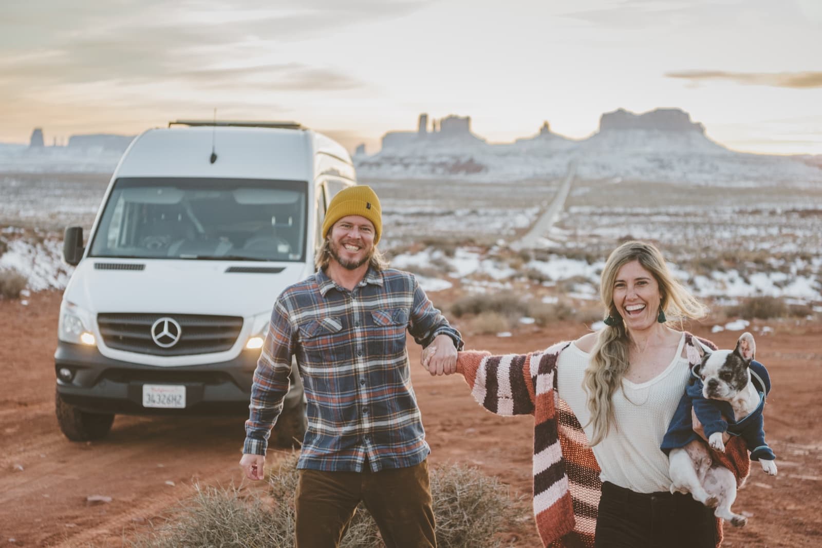 Michael and Renee holding hands in front of their camper van in Monument Valley — tap to play the intro video