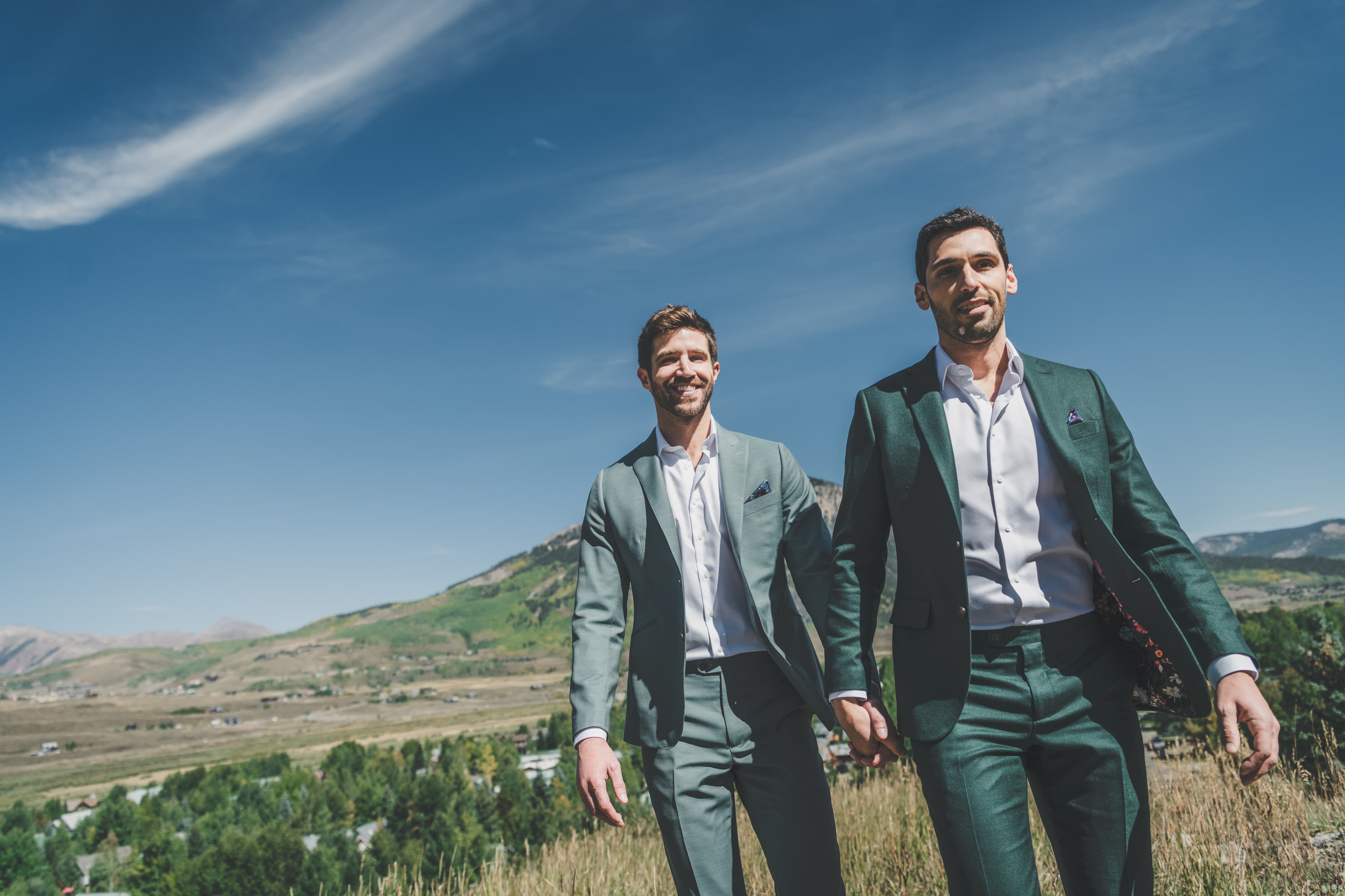 Greg and John walking hand in hand through tall grass with the Elk Mountains beyond