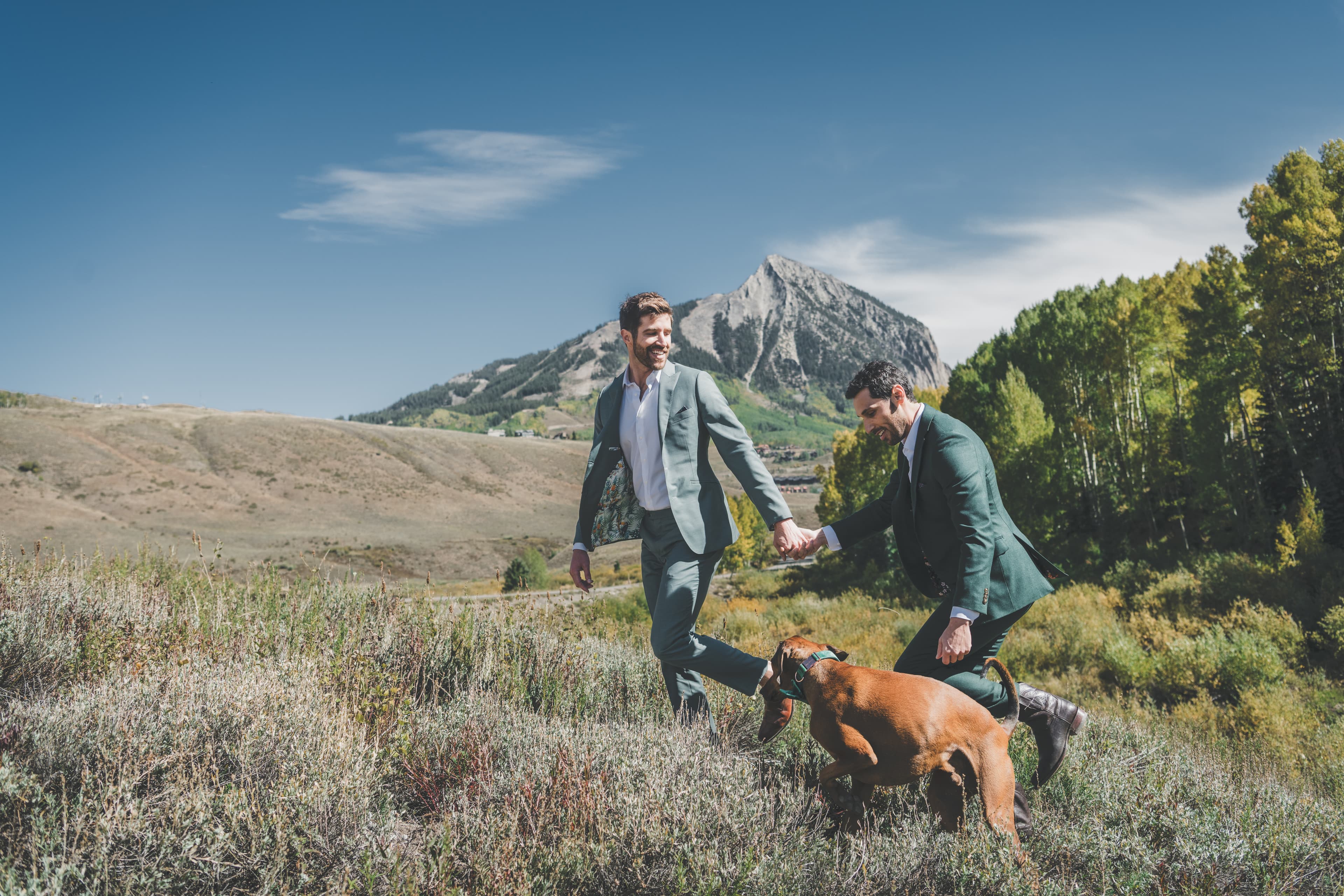 Greg and John walking with their dog through tall grass at the base of Mt. Crested Butte