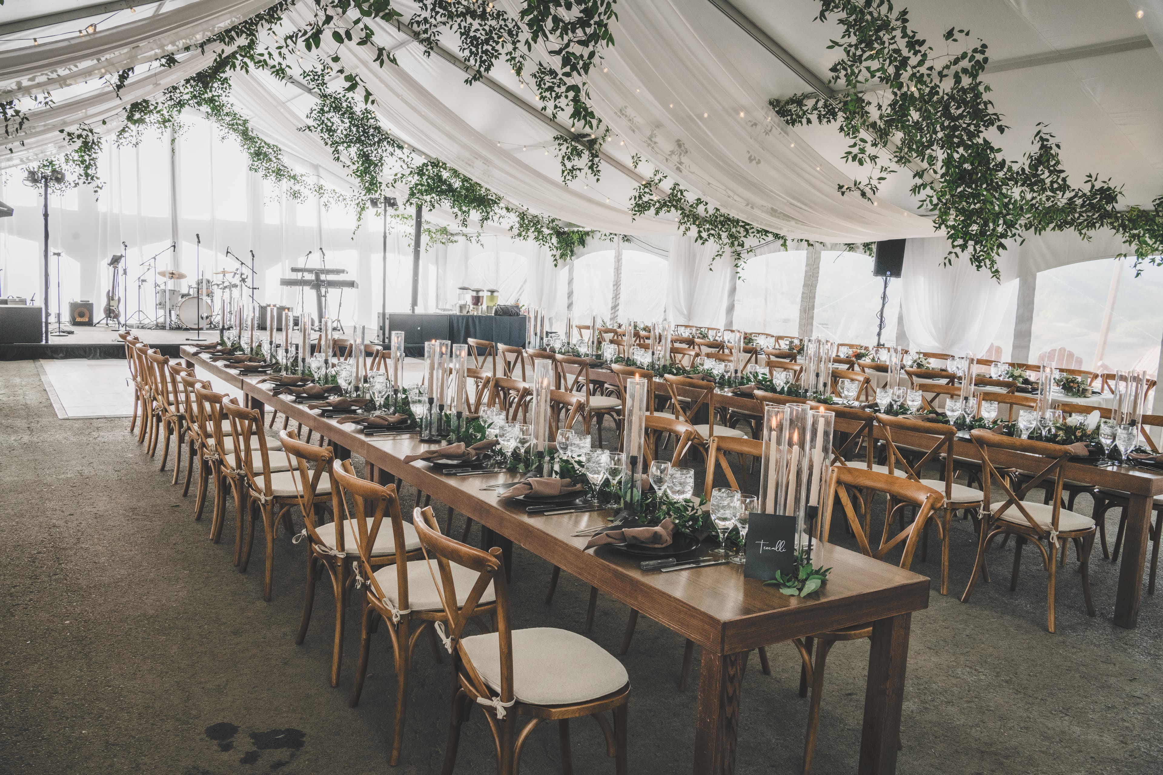 Wide view of Greg and John's reception tent with long tables and greenery draped from the ceiling