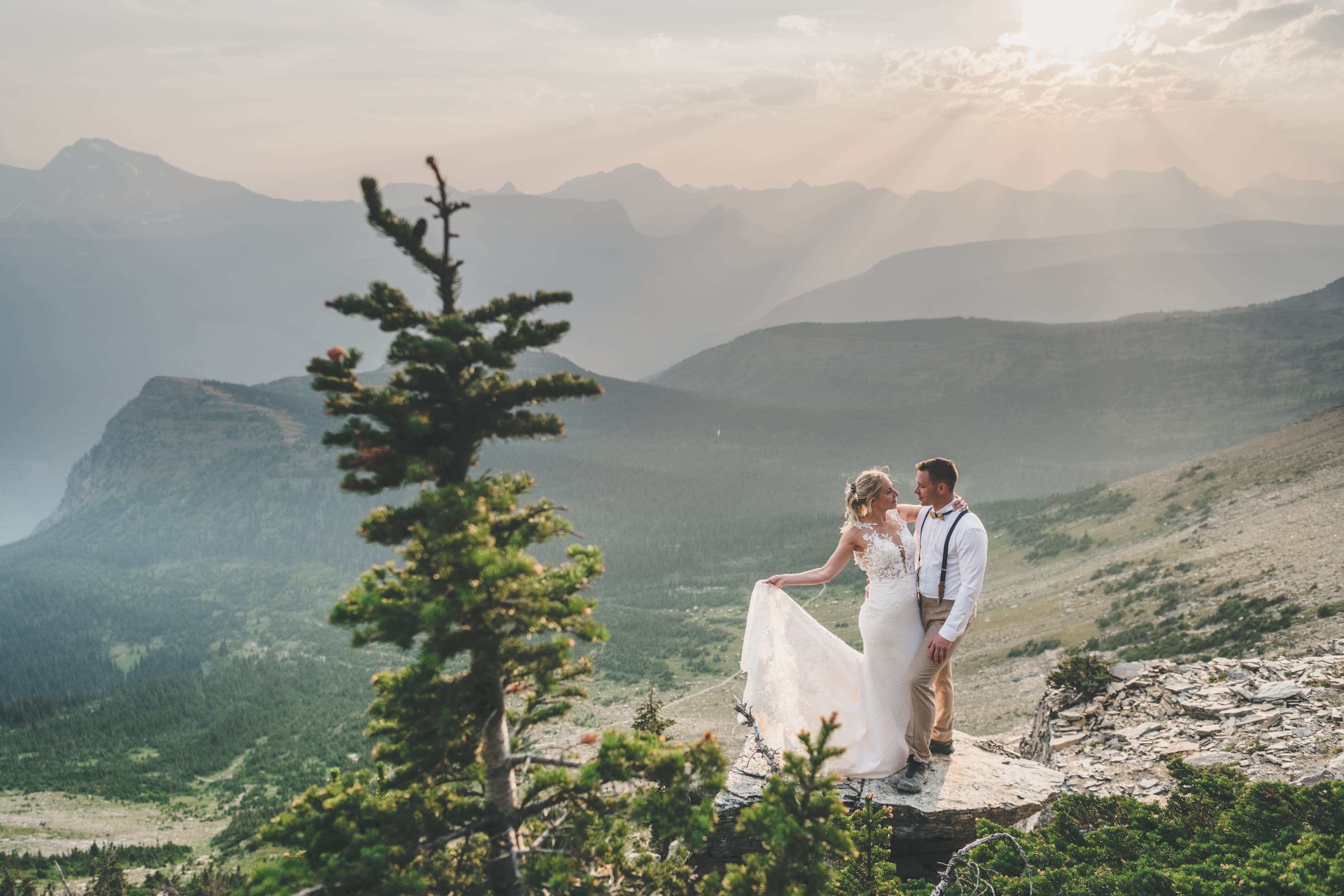 Shawna and Ryan on a rocky outcrop as sunset light beams break across Glacier National Park