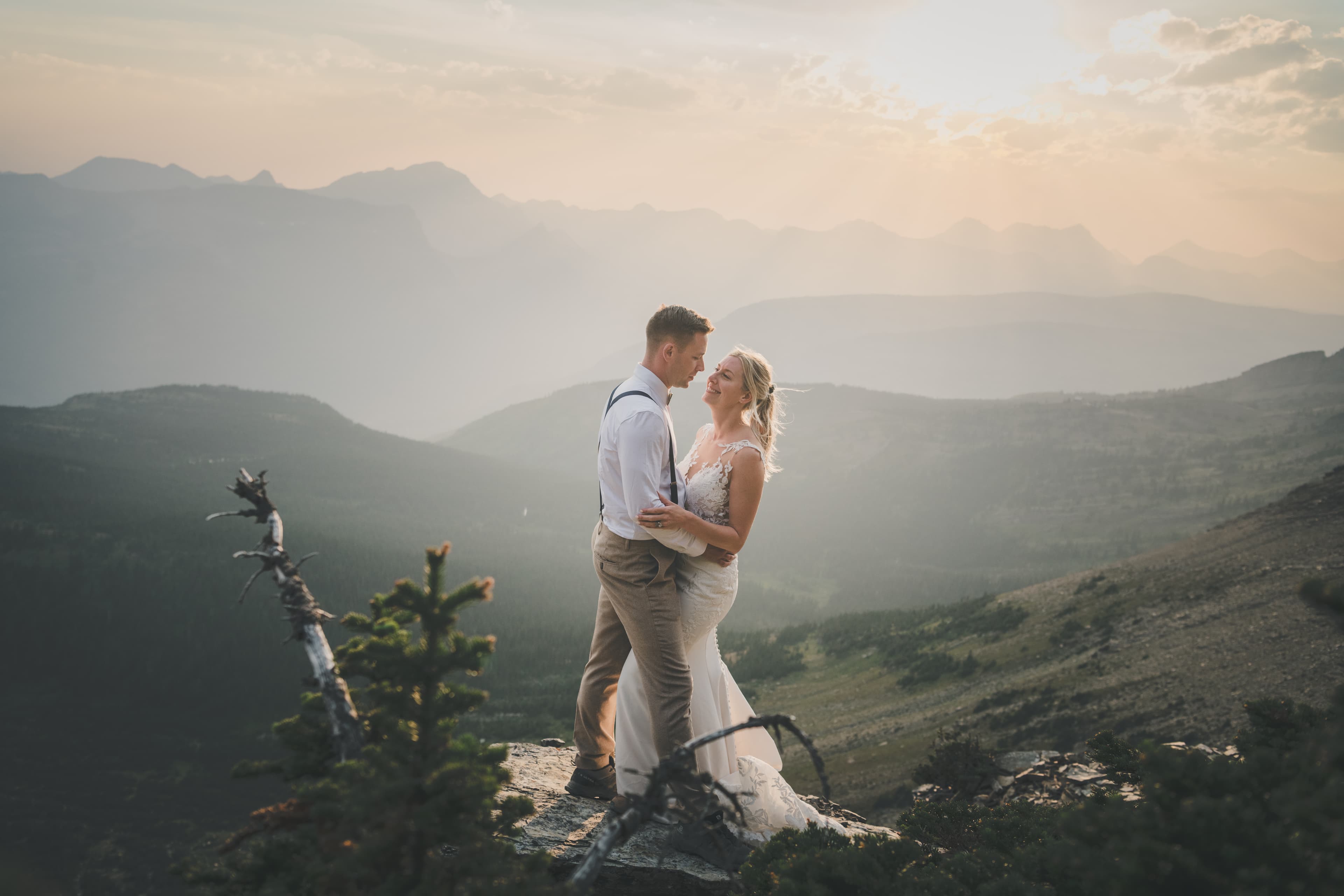 Shawna and Ryan facing each other at golden hour with Glacier's layered ridges fading into the haze