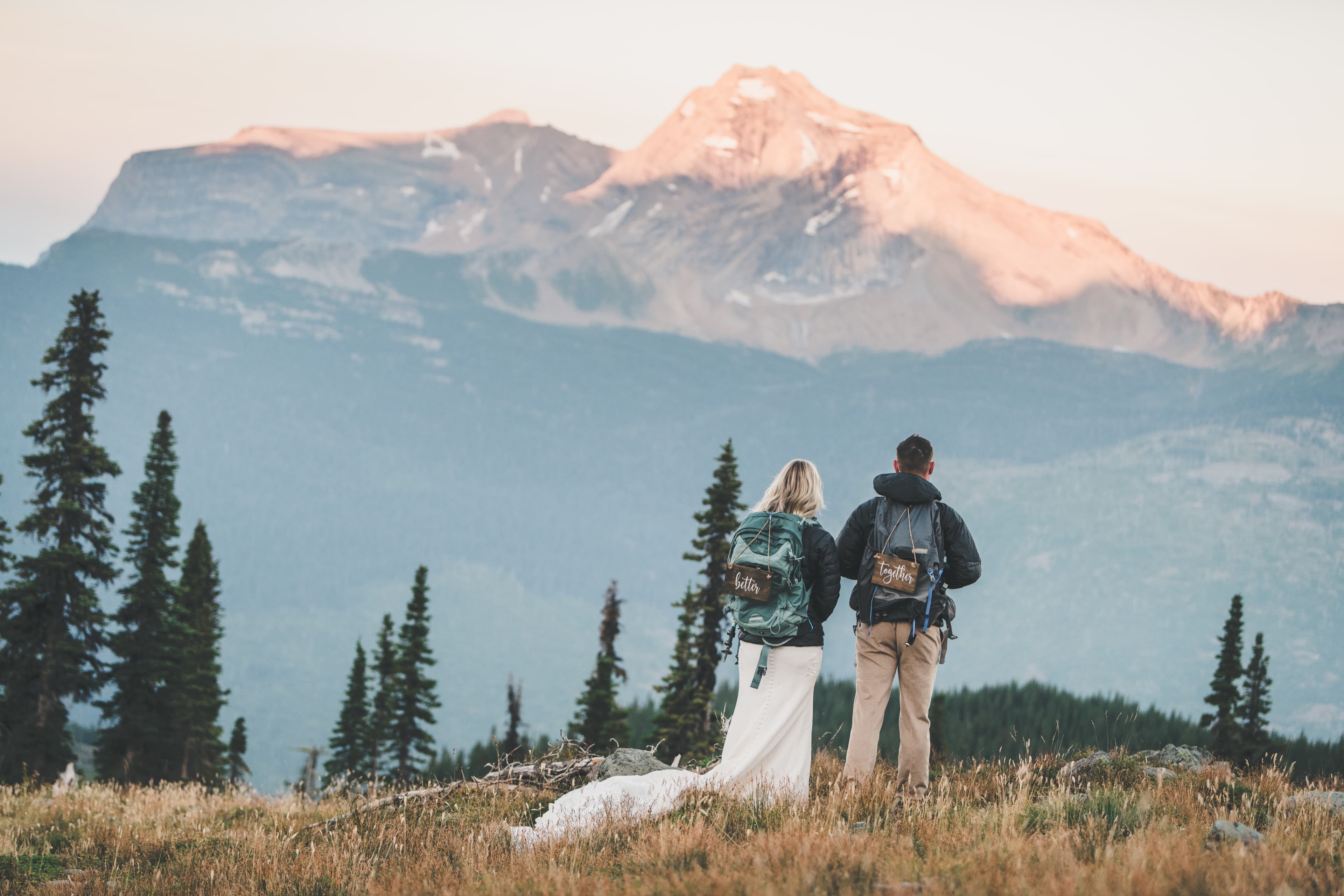 Shawna and Ryan from behind with their 'Better' and 'Together' backpacks looking at an alpenglow peak