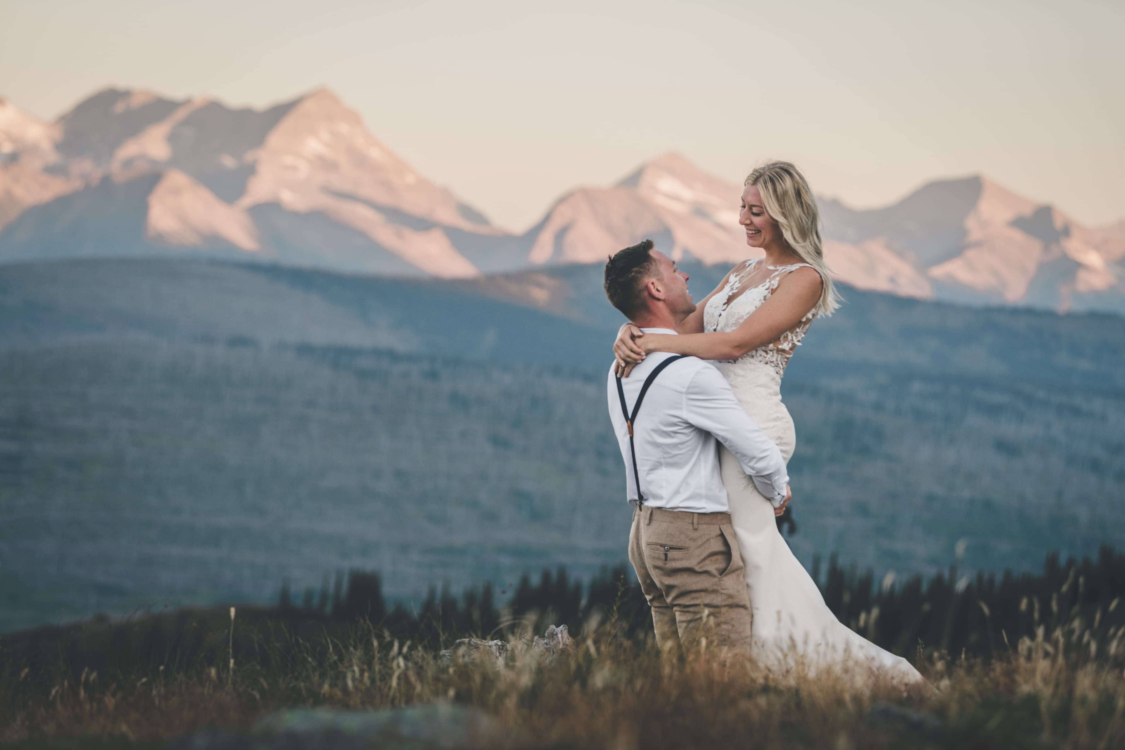 Ryan lifting Shawna at sunset on the ridge with alpenglow peaks lining the horizon behind