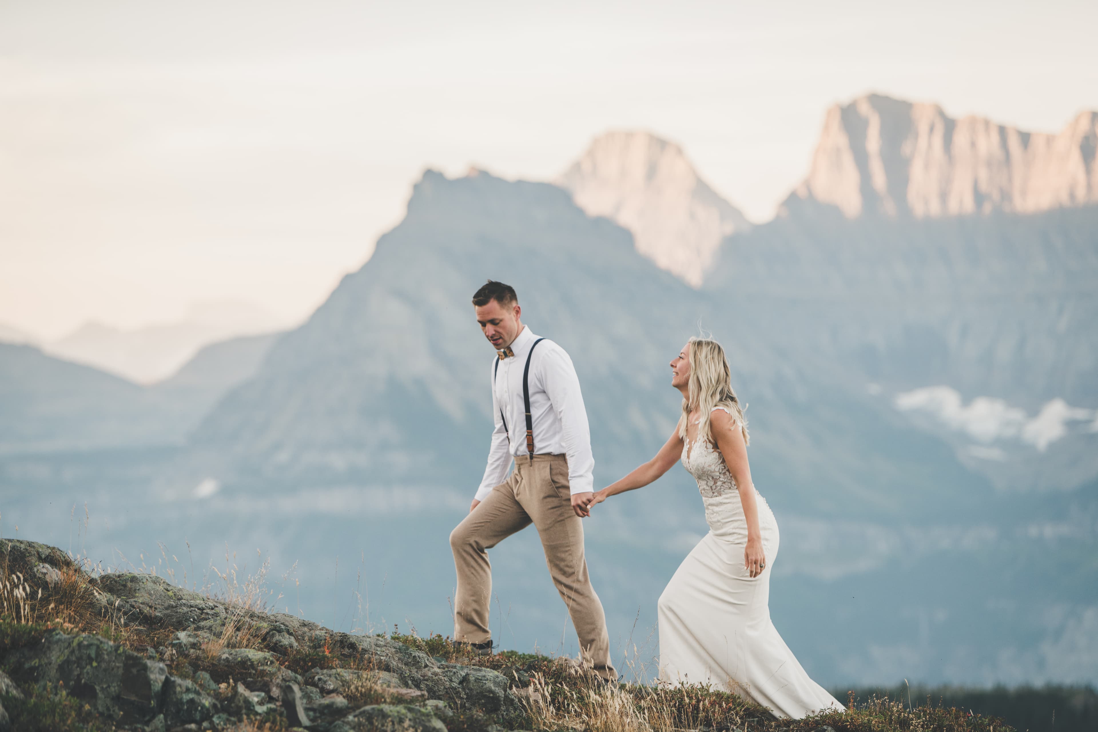 Shawna and Ryan hand-in-hand stepping along the ridge spine with peaks layering behind