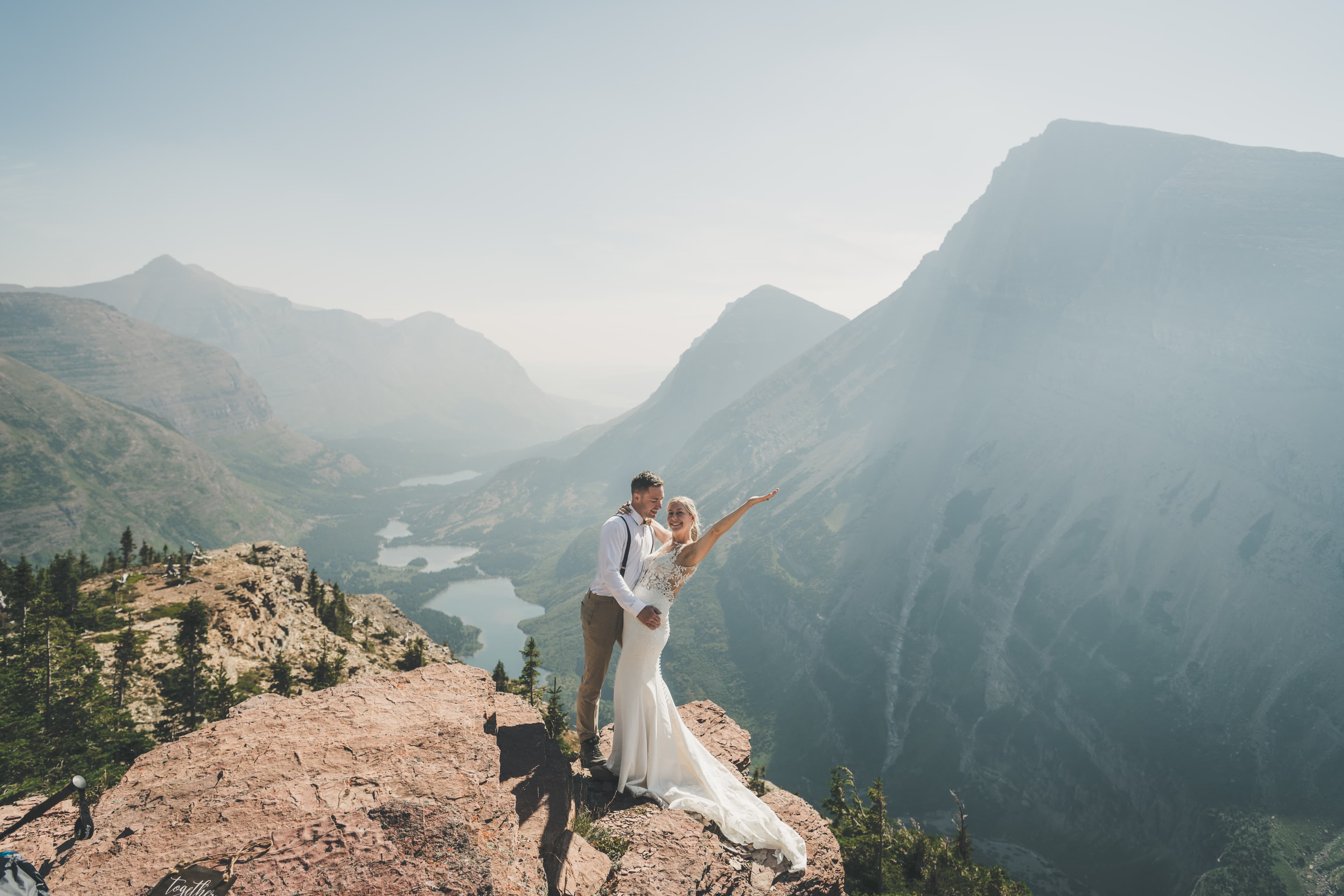 Shawna raising her arm in celebration on a rocky outcrop above the Many Glacier valley with Ryan beside her