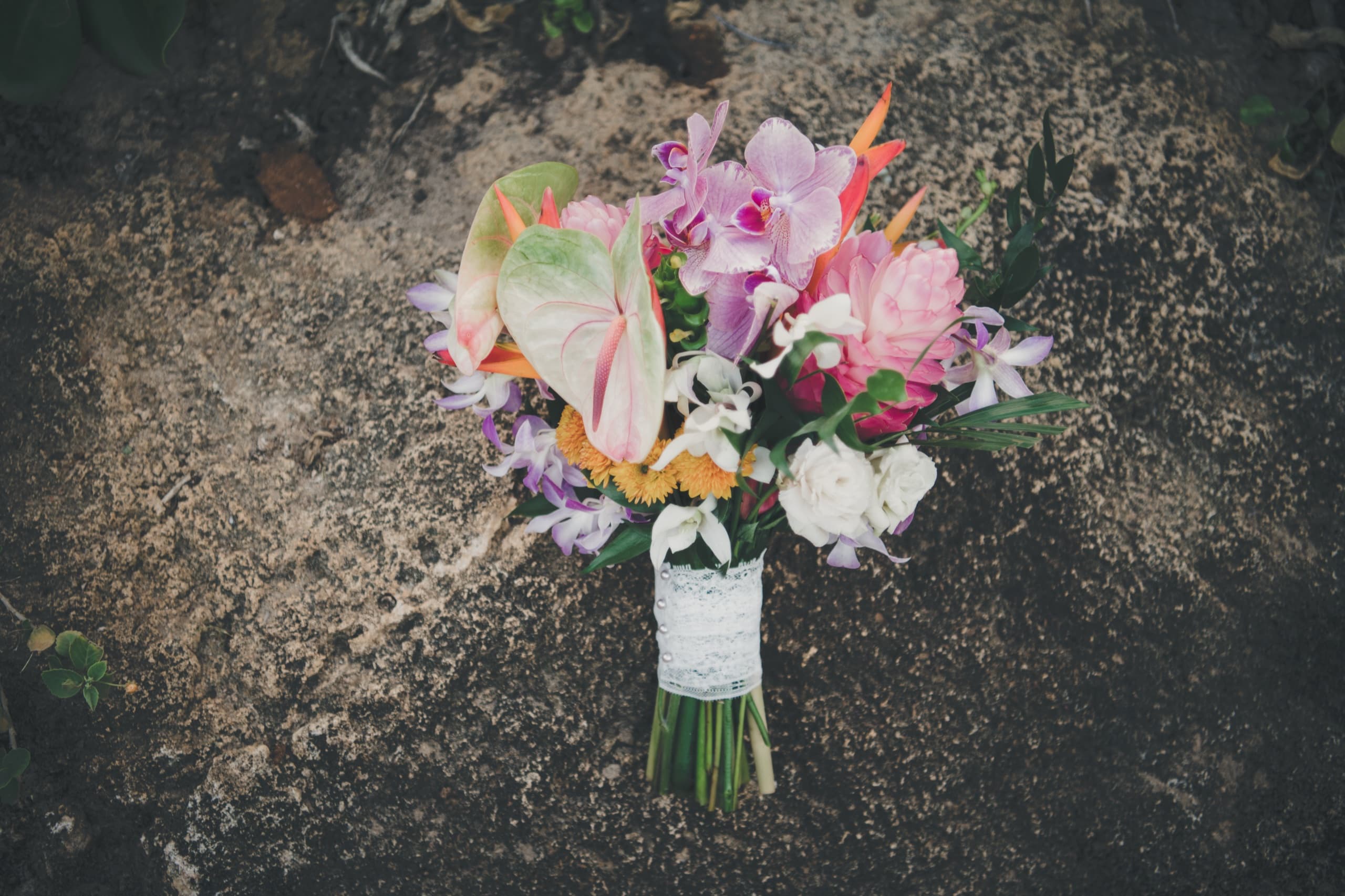 Erin's tropical bouquet — anthurium, orchids, and ginger — resting on sandstone before the ceremony