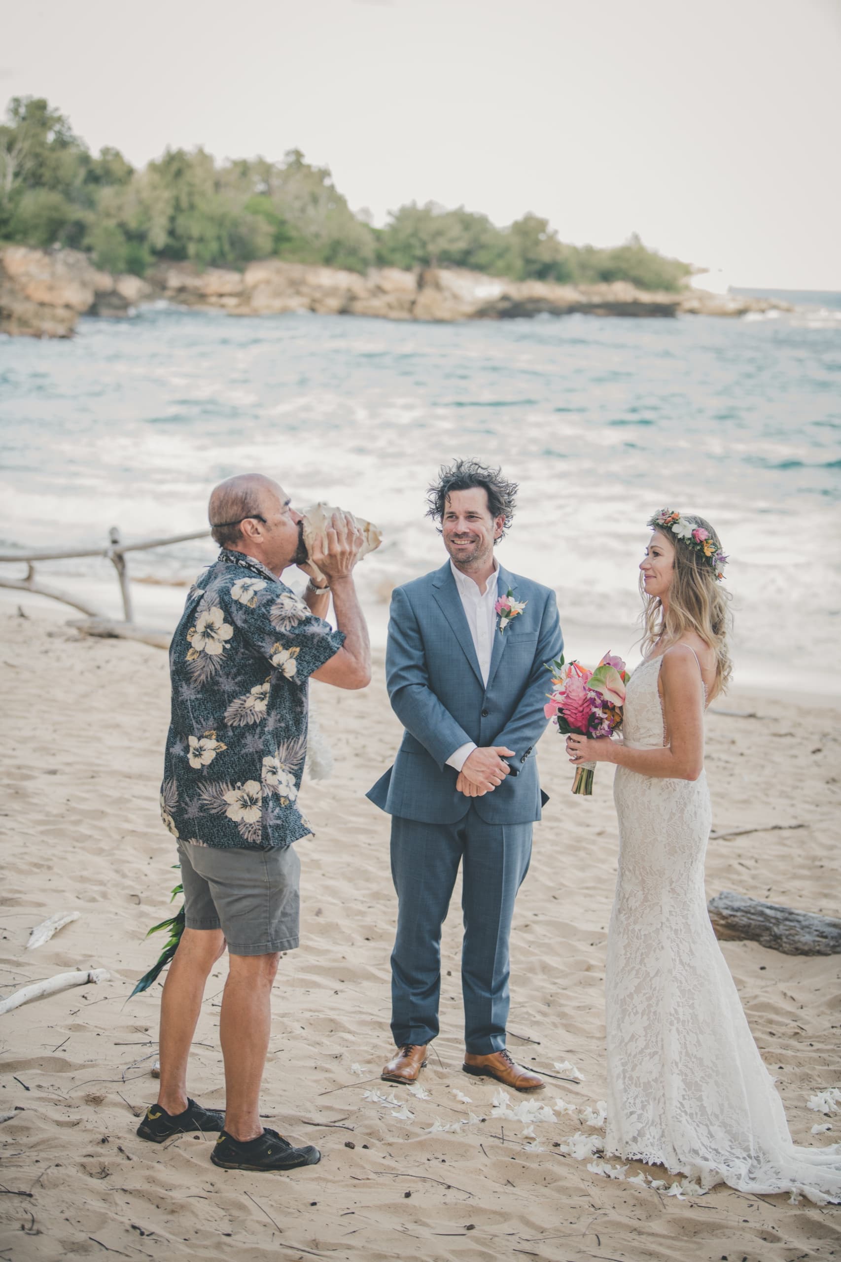 The officiant blowing a conch shell to open Erin and Kenny's Mahaulepu beach ceremony