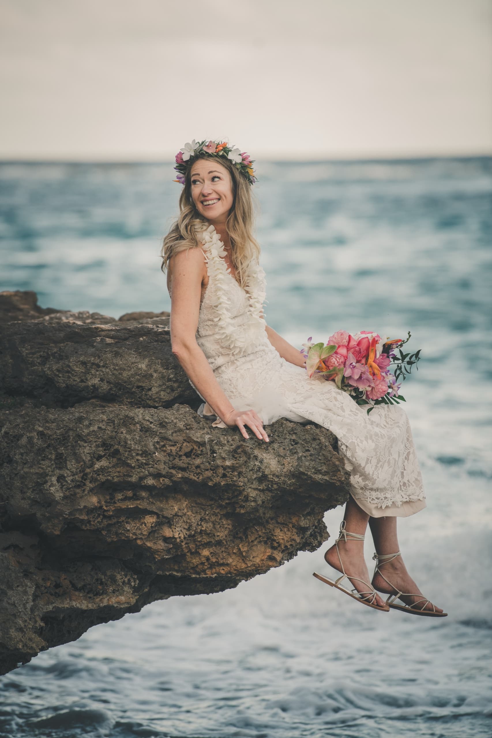 Erin sitting on the edge of a sandstone bluff with her bouquet, surf rolling below