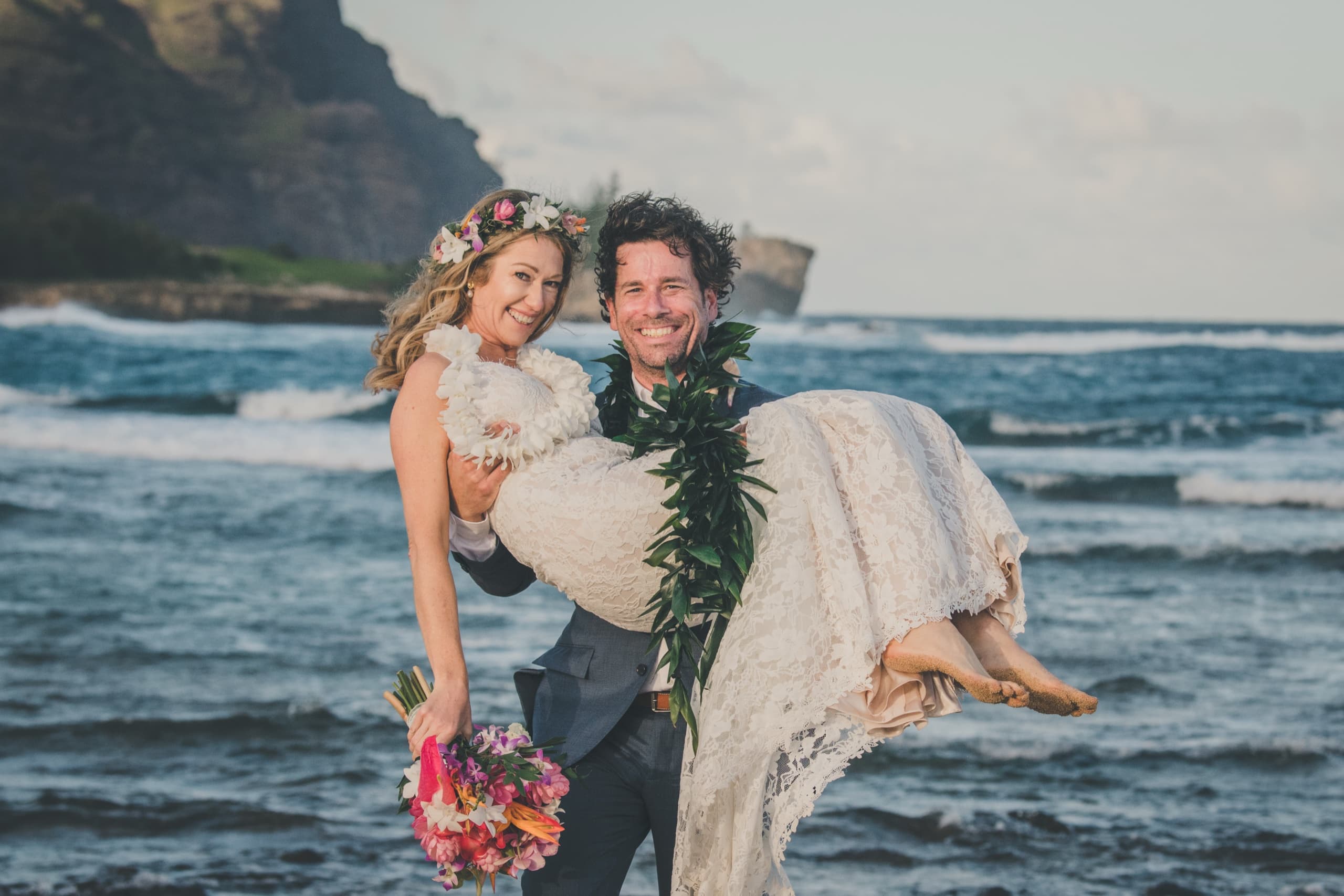Kenny carrying Erin across the beach in his arms with the Na Pali ridge in the distance