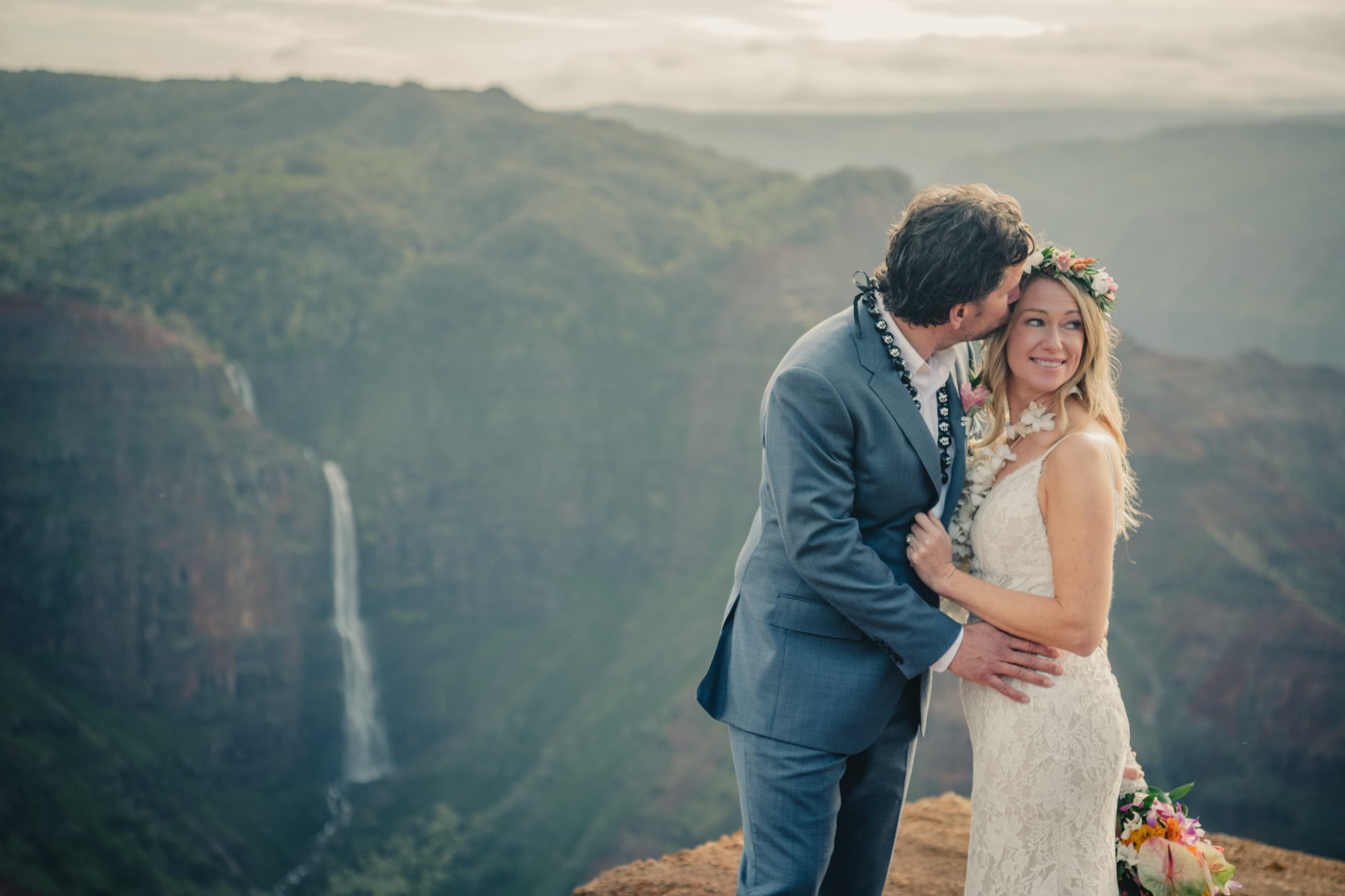 Kenny kissing Erin's forehead at the rim of Waimea Canyon with Waipoo Falls dropping behind them