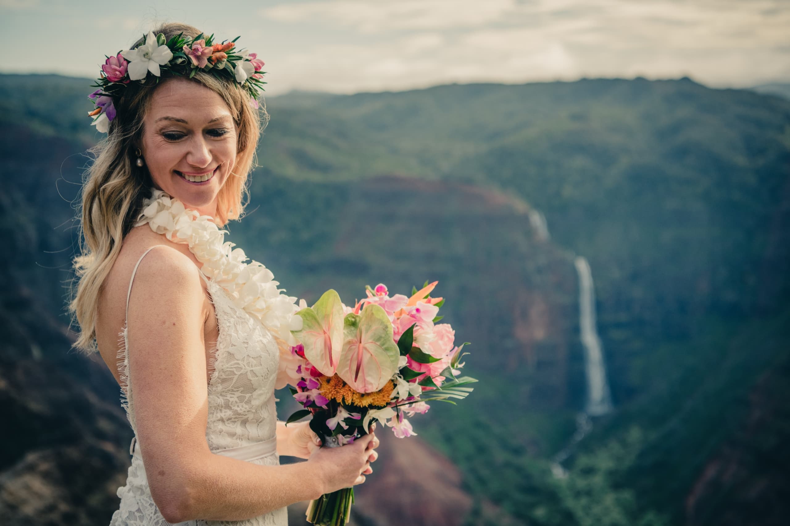 Close-up of Erin holding her tropical bouquet with the cliffs and waterfalls of Waimea Canyon behind her
