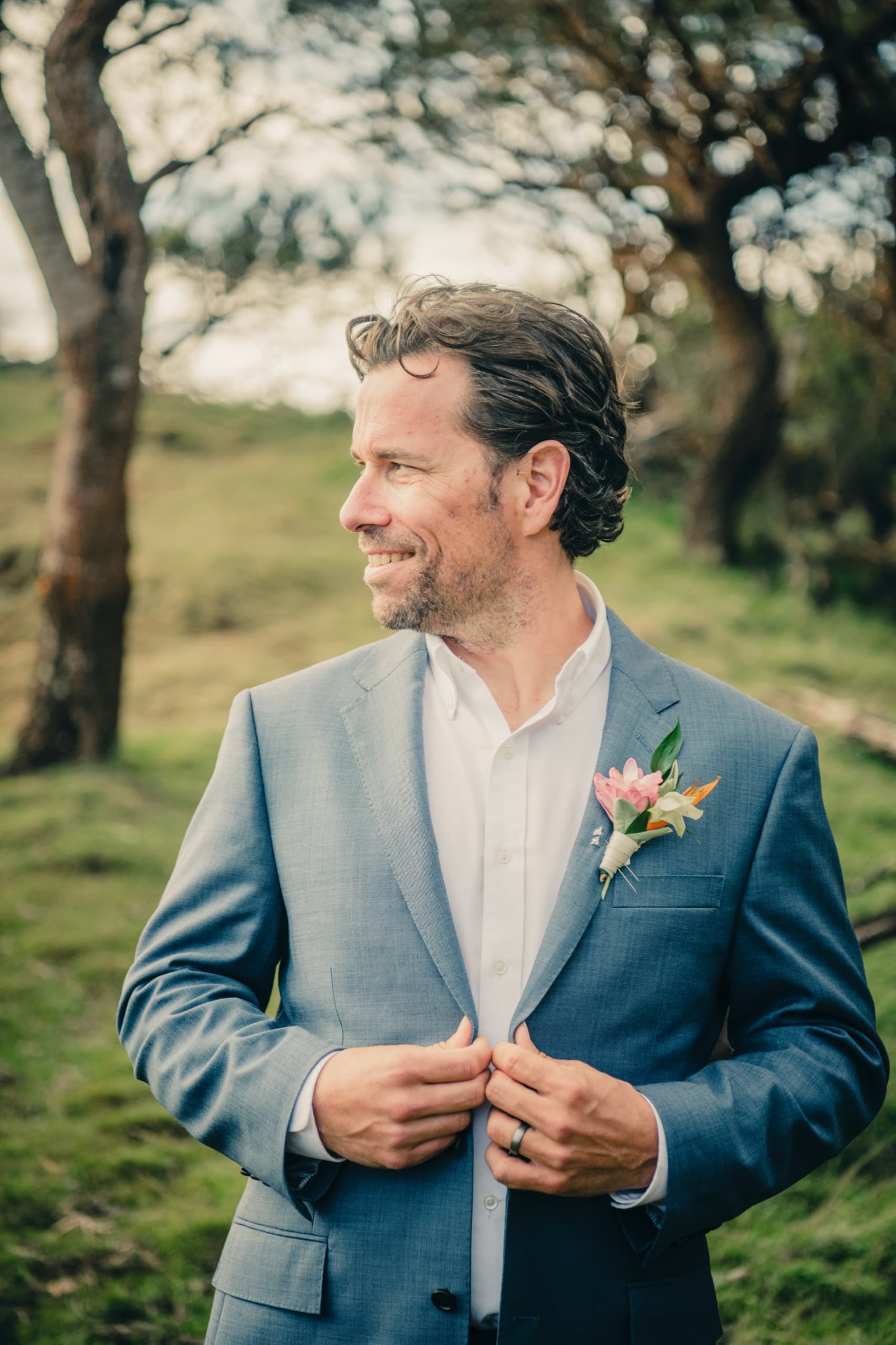 Kenny in his blue suit and tropical boutonniere standing alone in a grassy field on the drive home