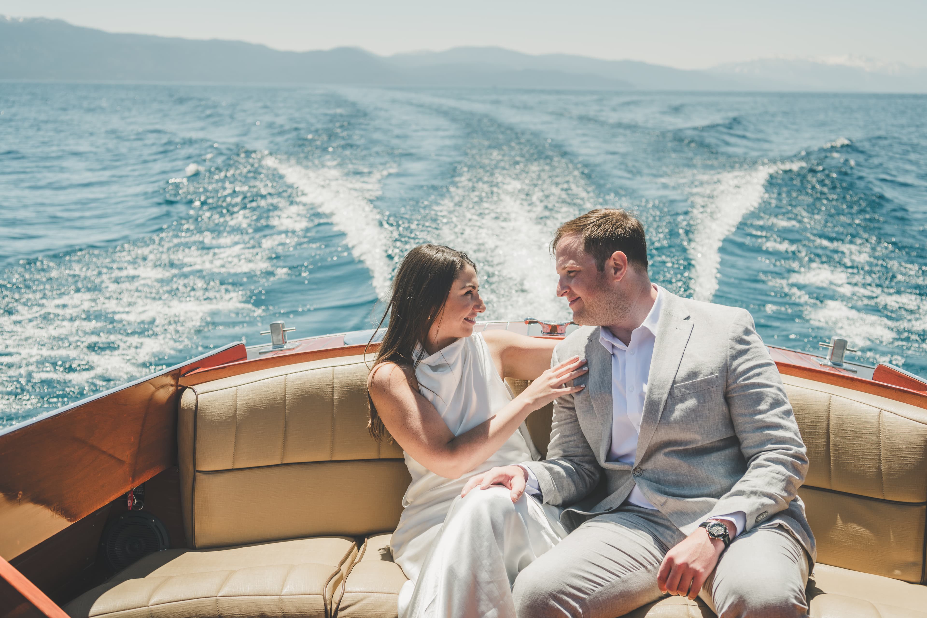 Hannah and Will on the back bench of a wooden boat with Lake Tahoe's wake spraying behind them