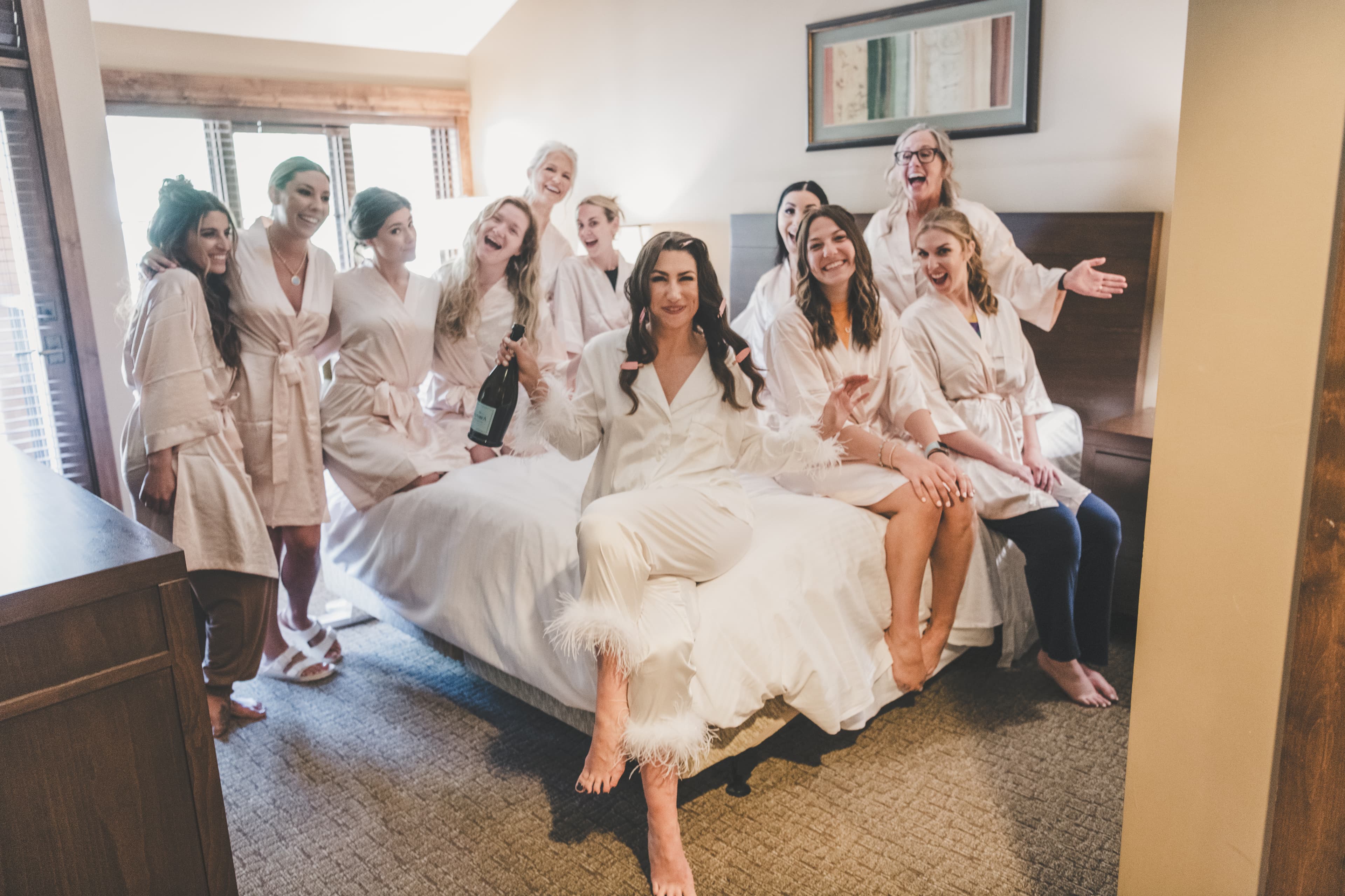 Hannah surrounded by her bridesmaids in matching robes laughing on the suite bed at Everline Resort