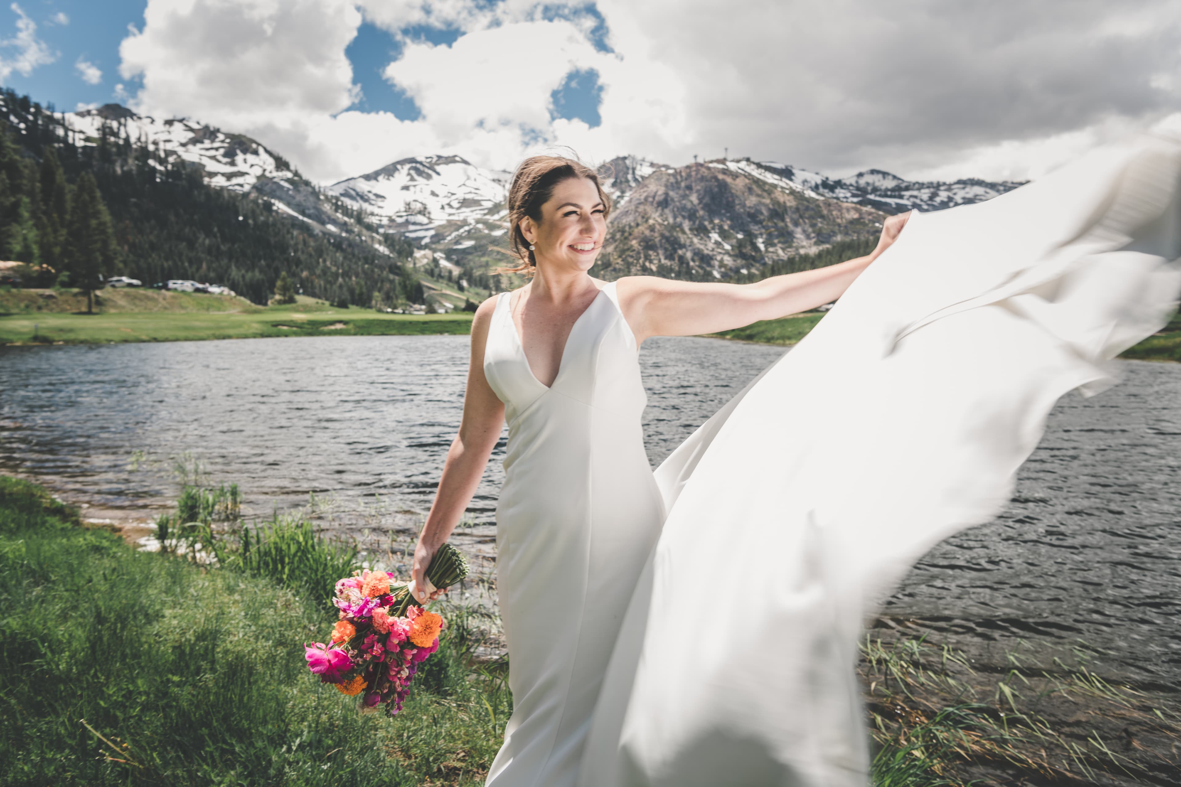 Hannah holding her marigold and peony bouquet, dress catching the wind, Olympic Valley peaks behind her