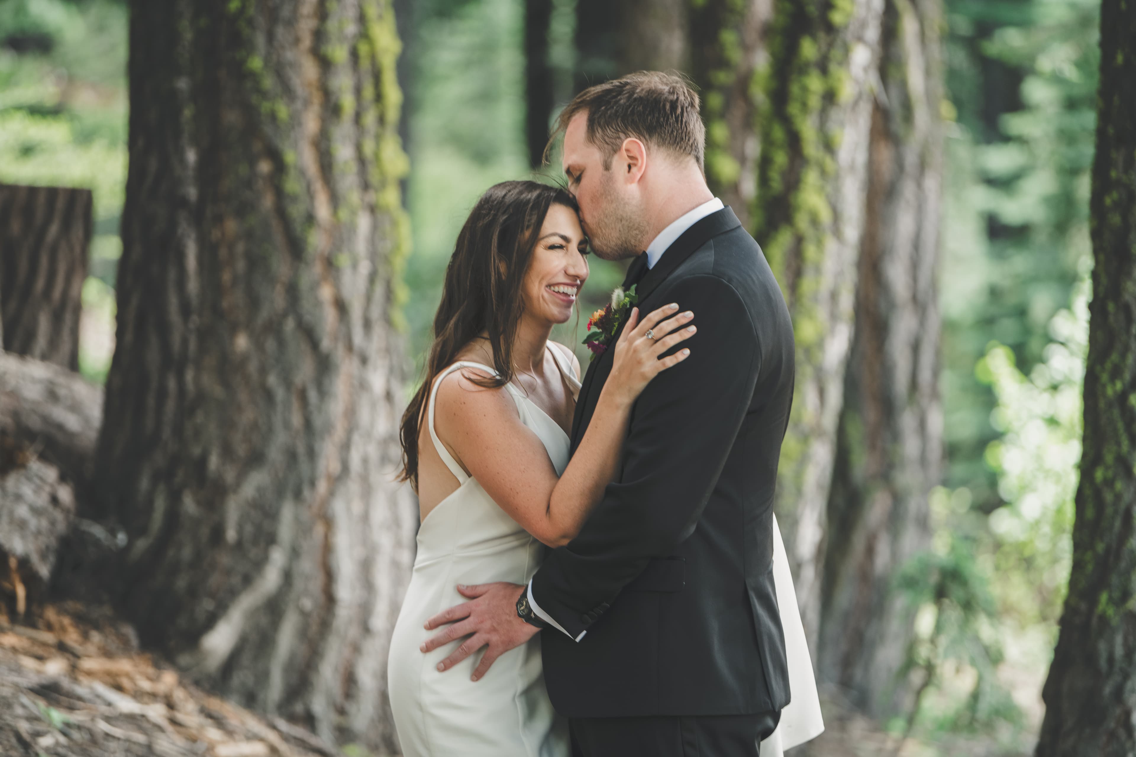 Will kissing Hannah's forehead as she laughs in the pine forest portrait session