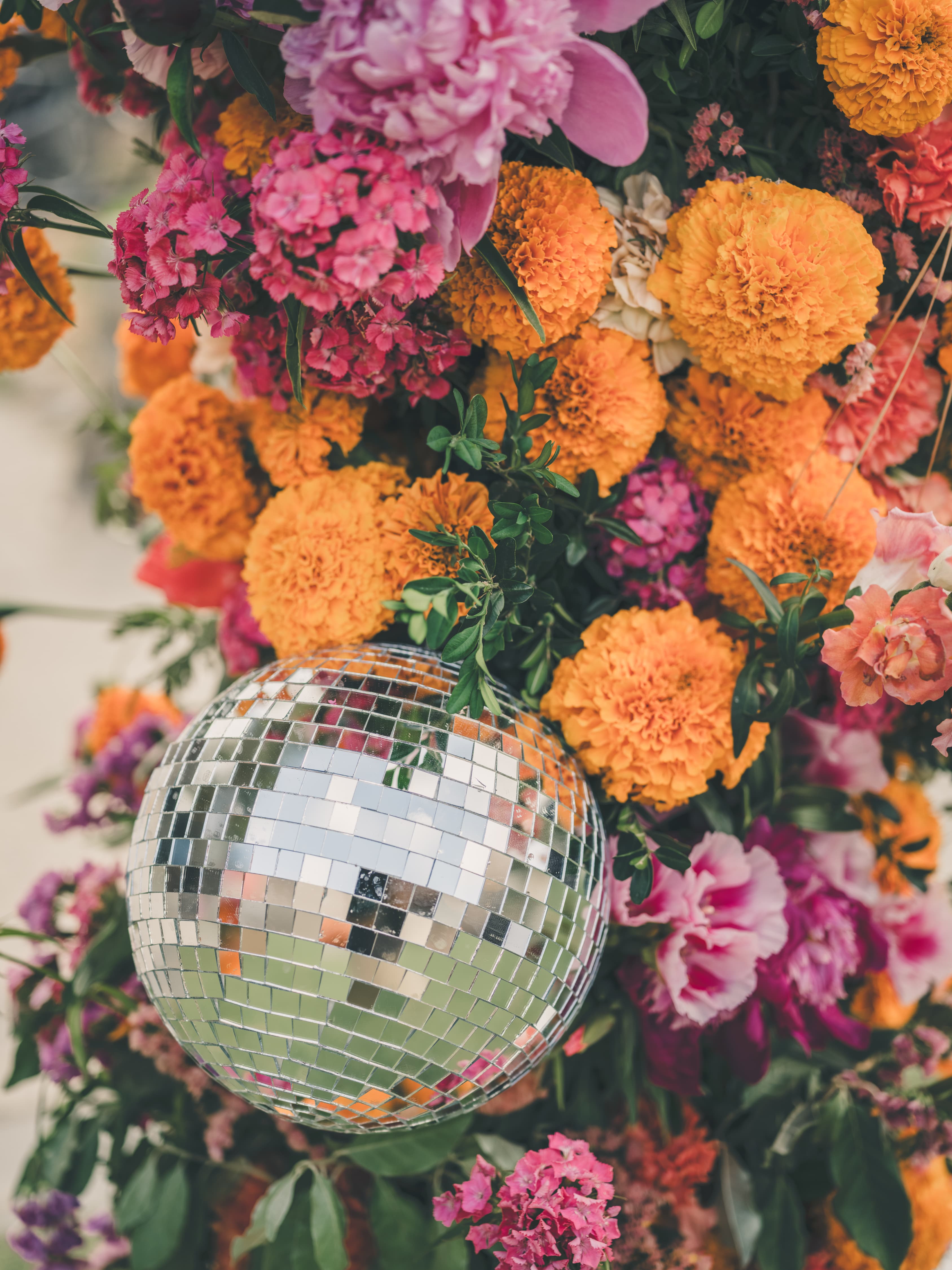 Reception detail of a hanging disco ball nestled into a wall of marigolds and peonies