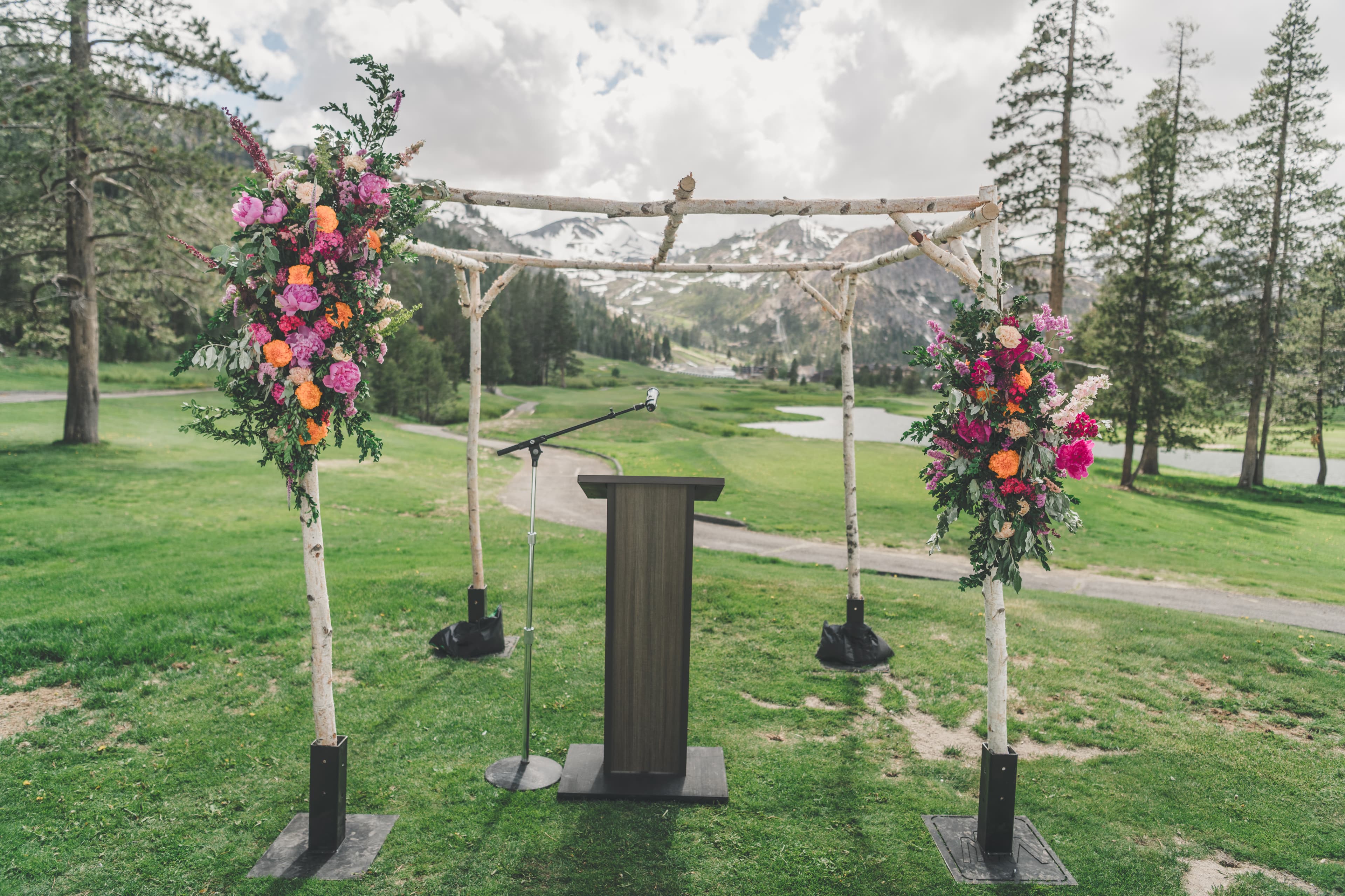 The birch ceremony arbor at Everline with marigolds and peonies, snow-streaked Palisades peaks behind