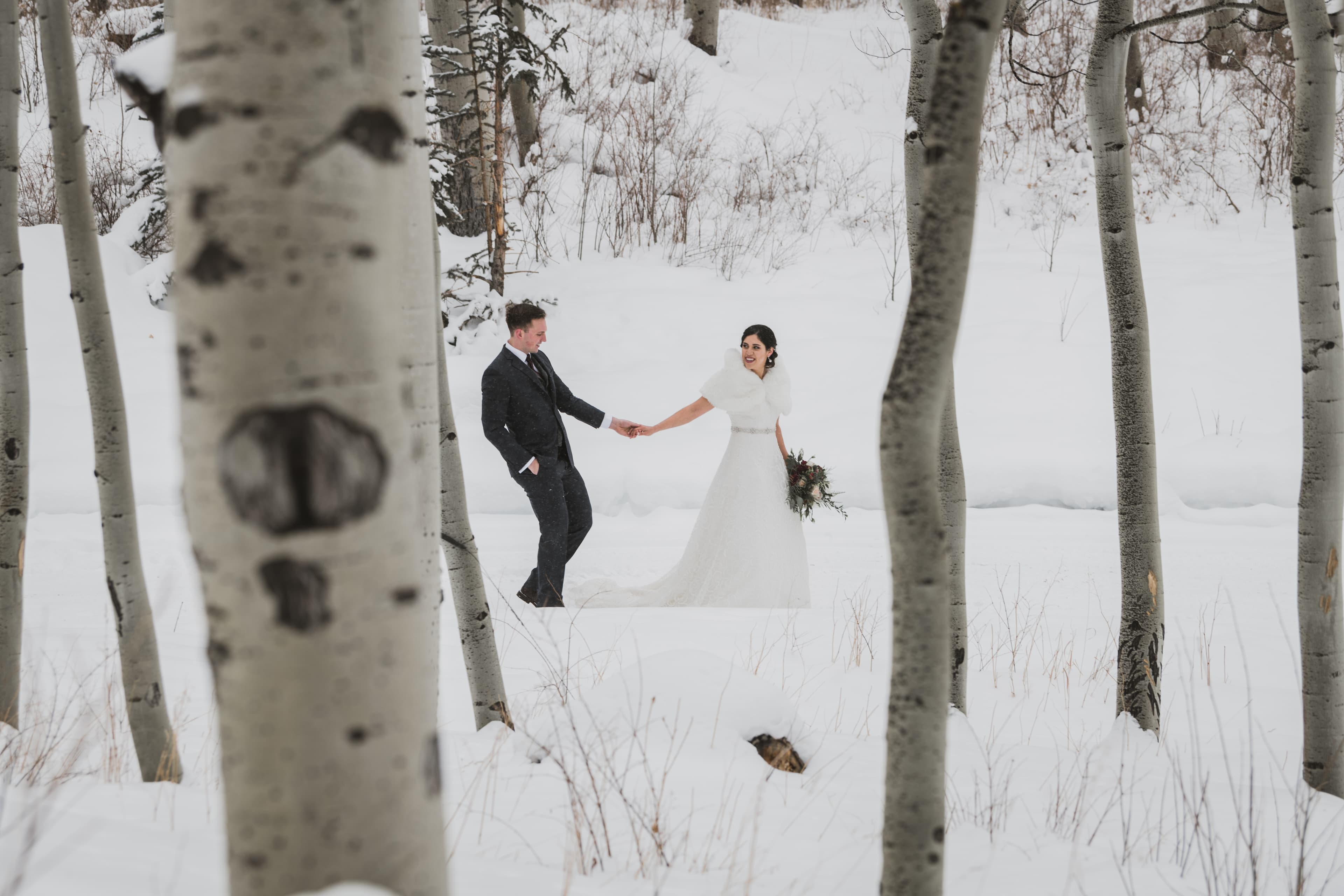 Sabrina and Patrick holding hands as they walk through snow framed by Telluride aspens