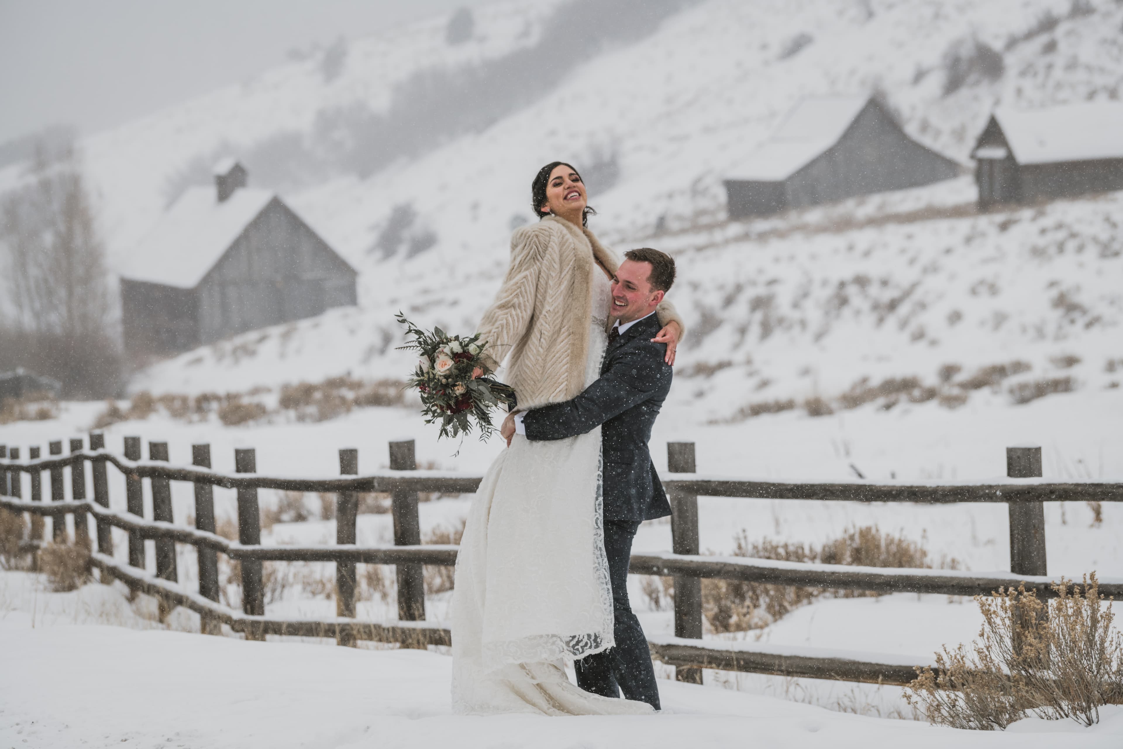 Sabrina and Patrick laughing in front of a snowy hillside with rustic barns above Telluride