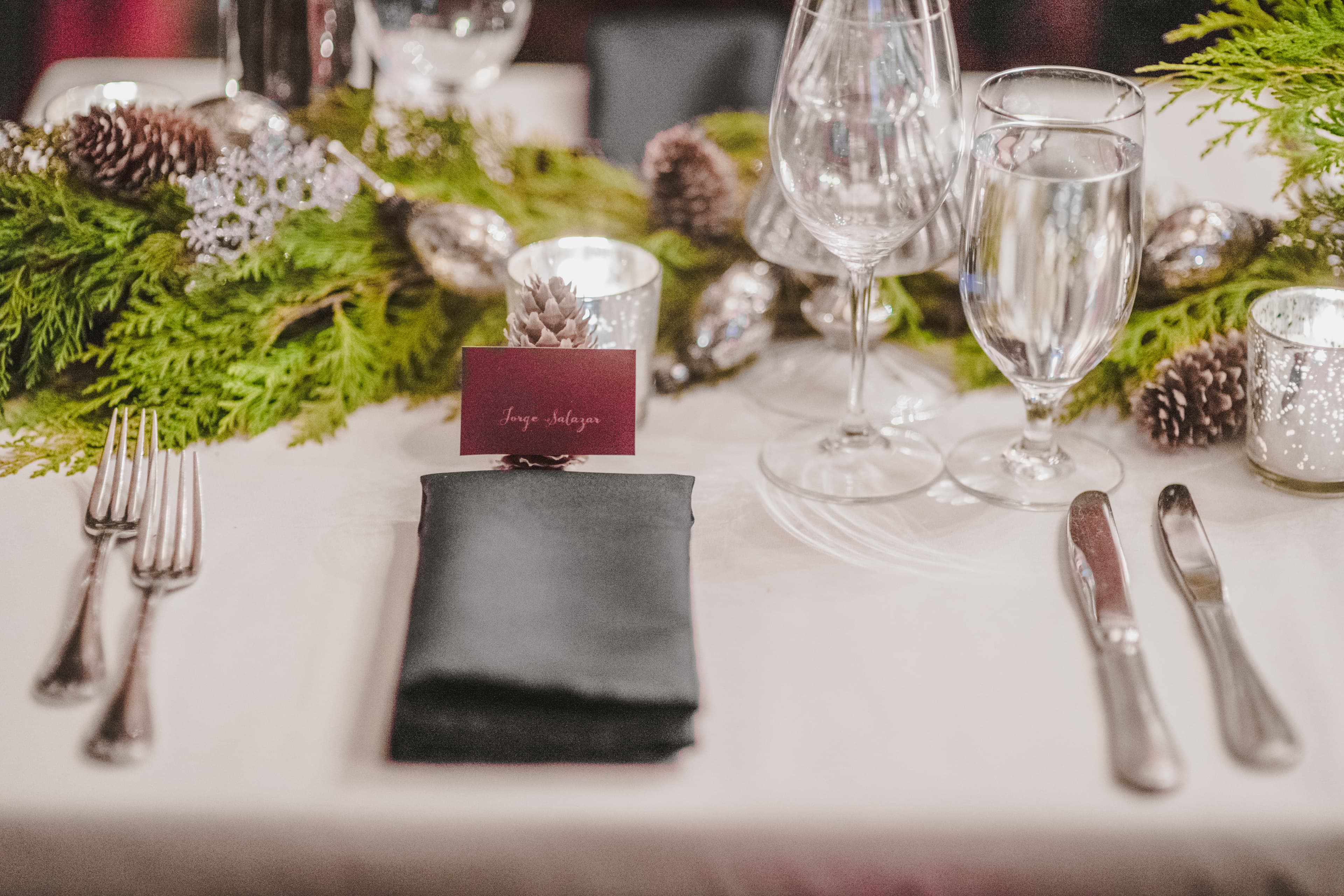 Place setting at Alpino Vino — burgundy escort card on a folded napkin with pinecone and cedar garland