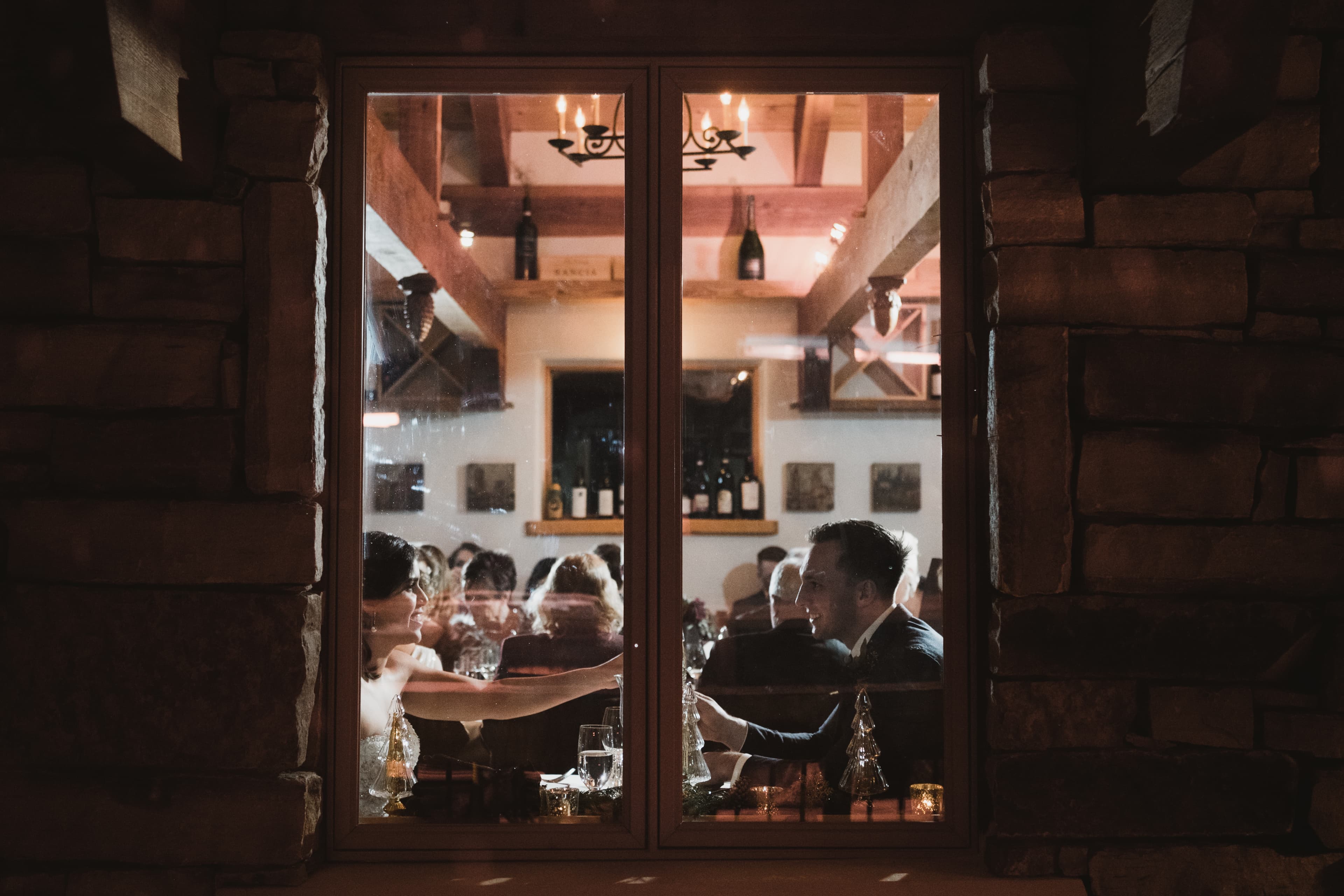 Sabrina and Patrick at their reception seen through the stone-framed window of Alpino Vino
