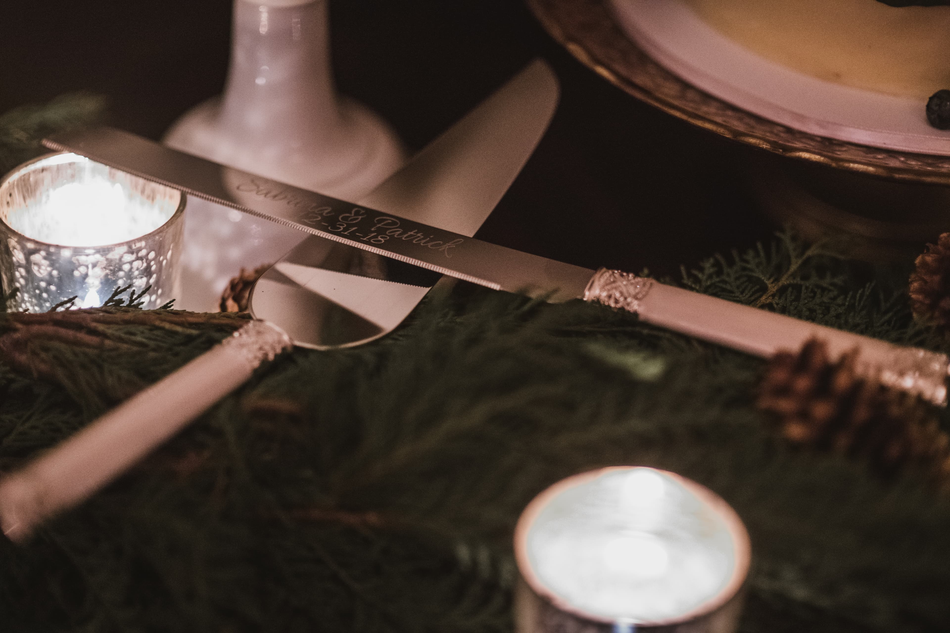 Personalized engraved cake knife for Sabrina and Patrick resting on cedar garland and candles