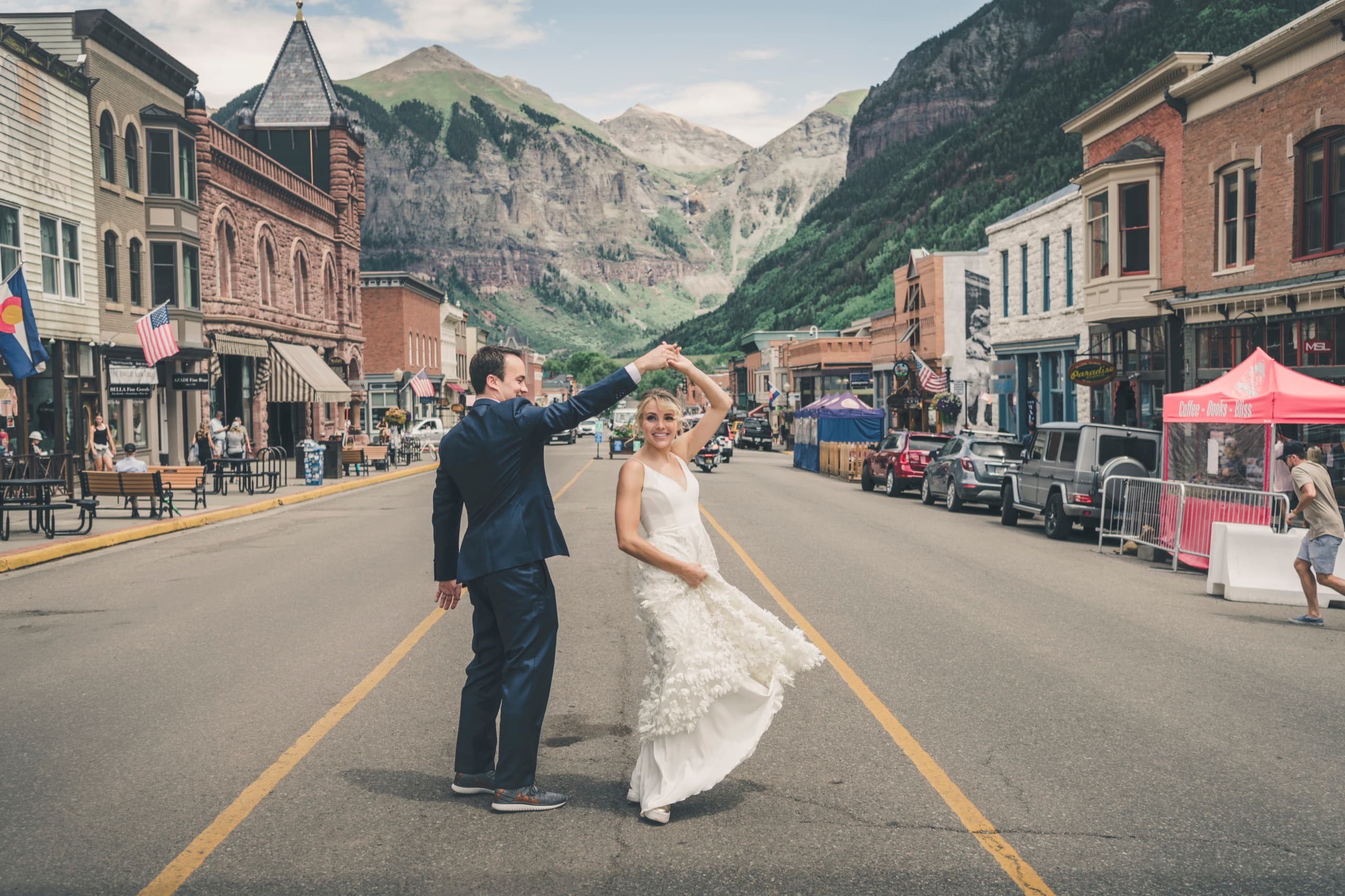 Meghan and Brent twirling on Telluride's main street with Victorian storefronts and the box canyon peaks behind them