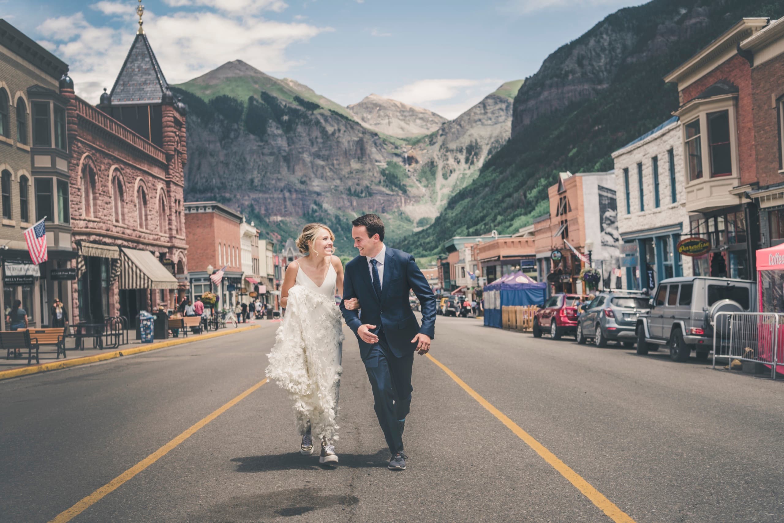 Meghan and Brent walking hand in hand laughing down Telluride main street with the mountains behind
