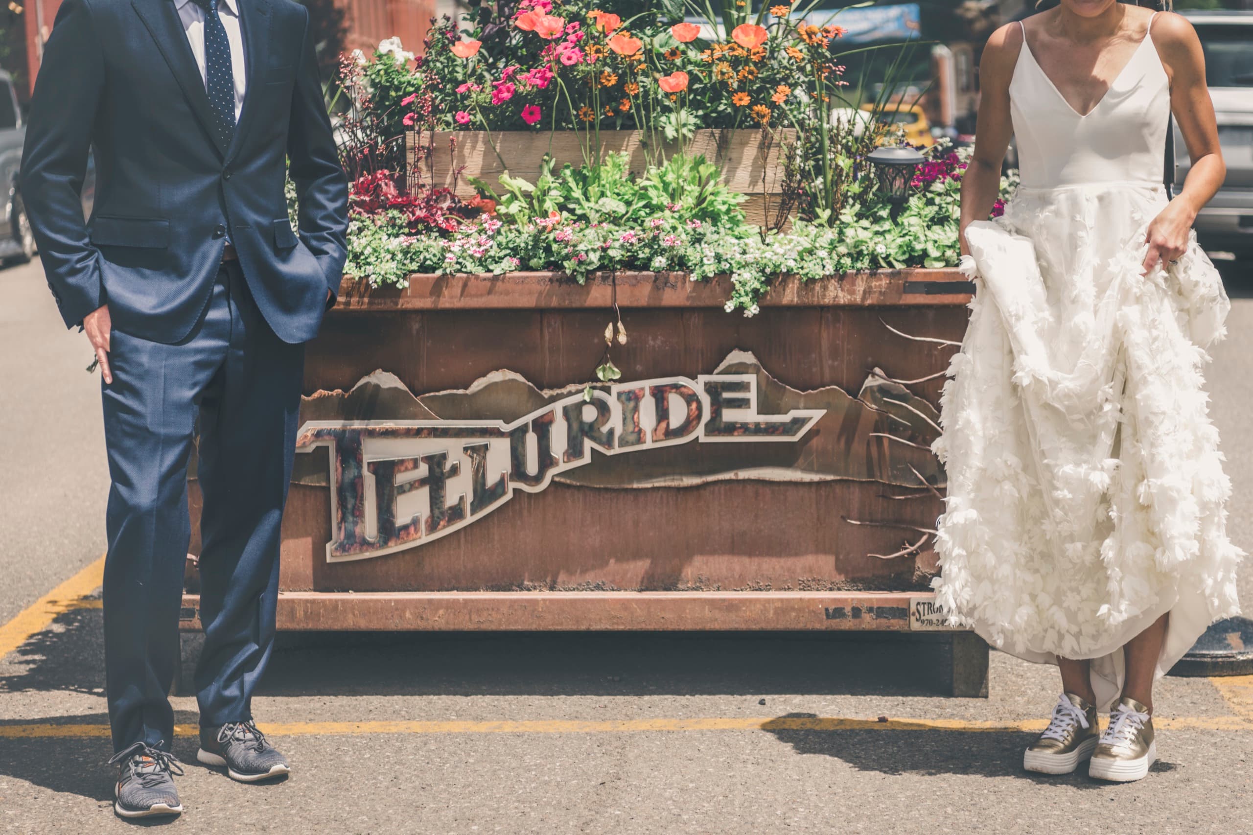 Meghan and Brent flanking a flowerbox sign in downtown Telluride, dress and suit in frame