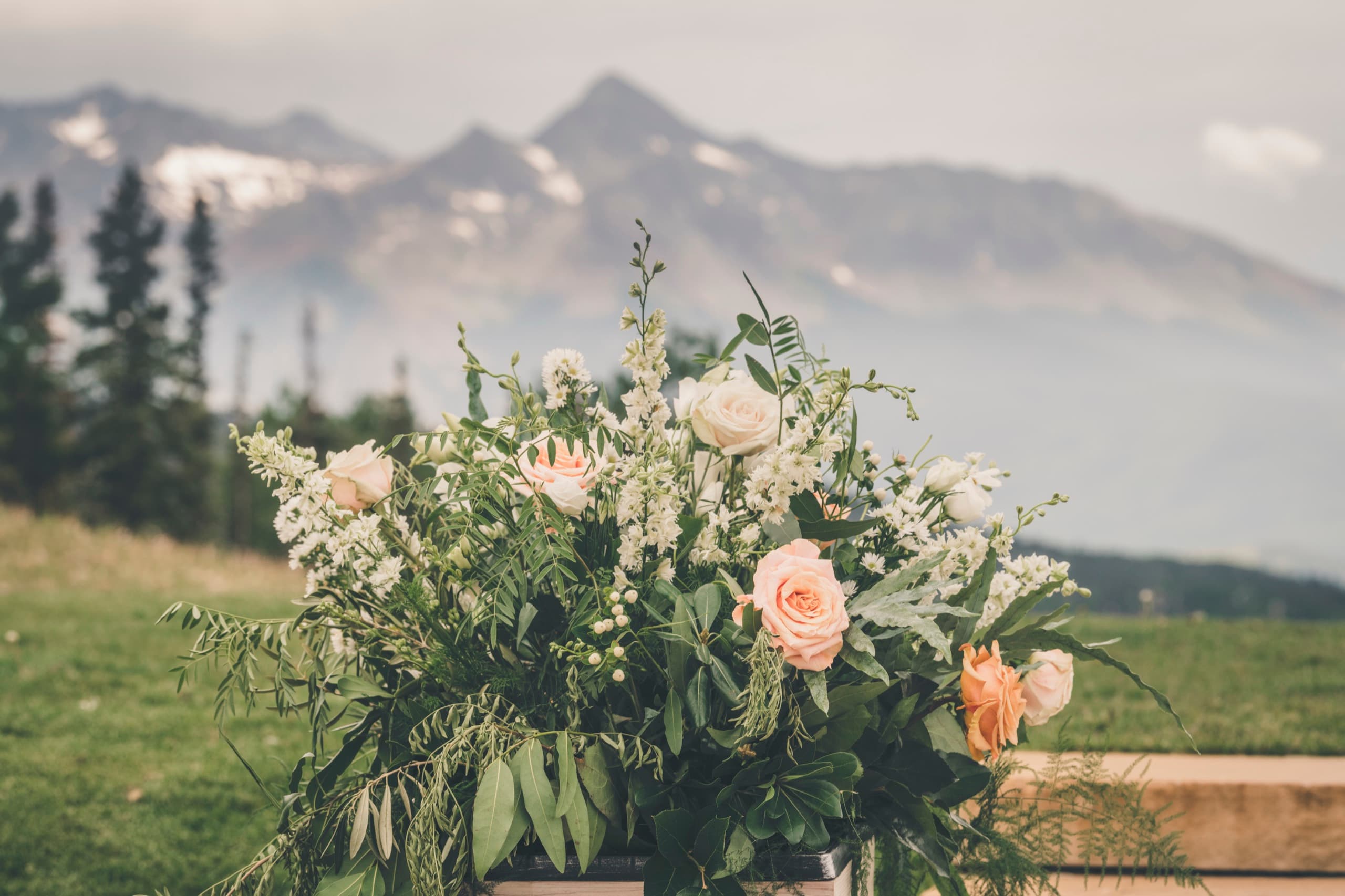 Detail of the peach and white ceremony floral arrangement with snowy peak behind at Gorrono Ranch