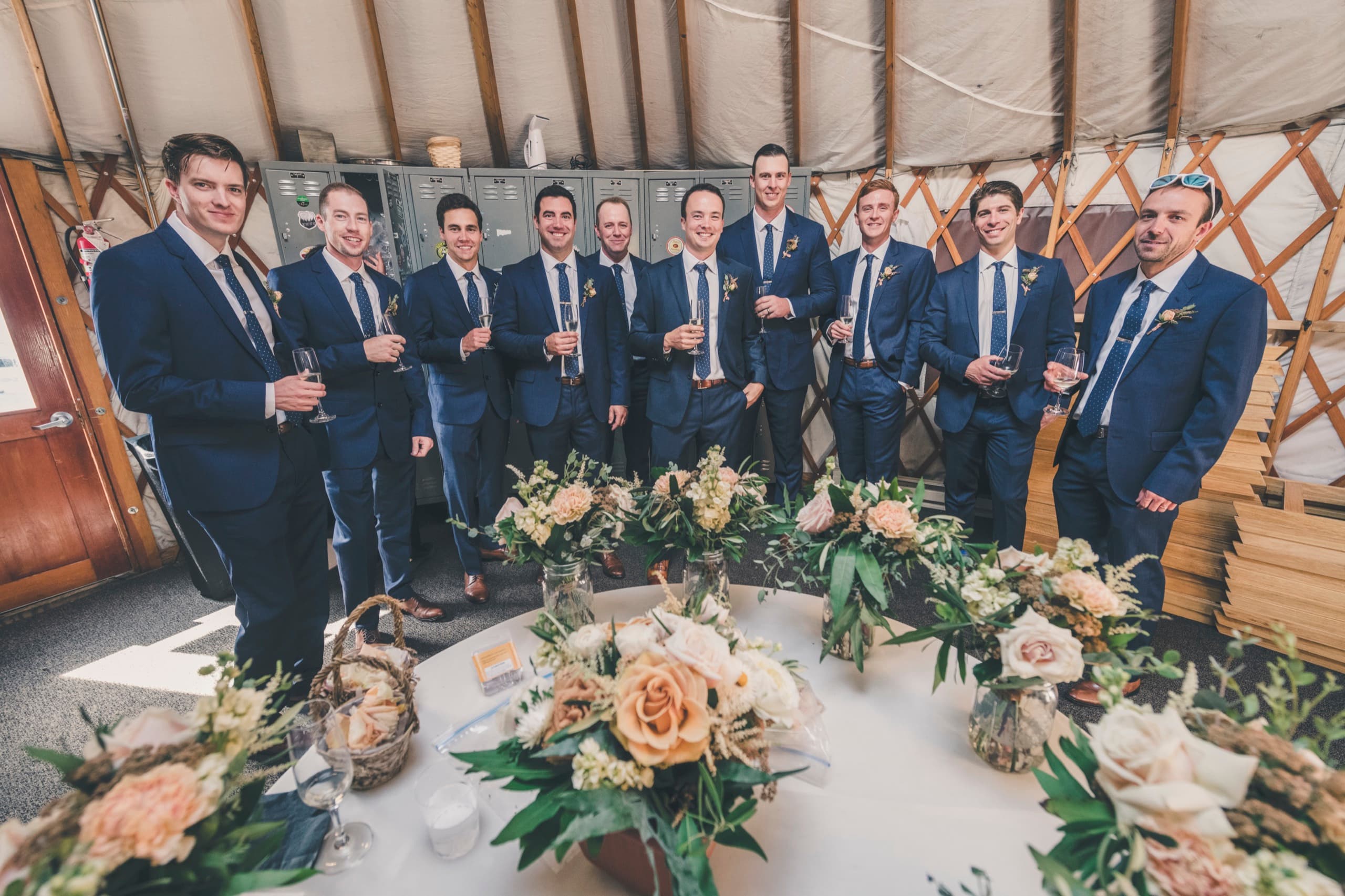Brent's groomsmen in navy suits posing with champagne in the prep yurt before the Gorrono Ranch ceremony