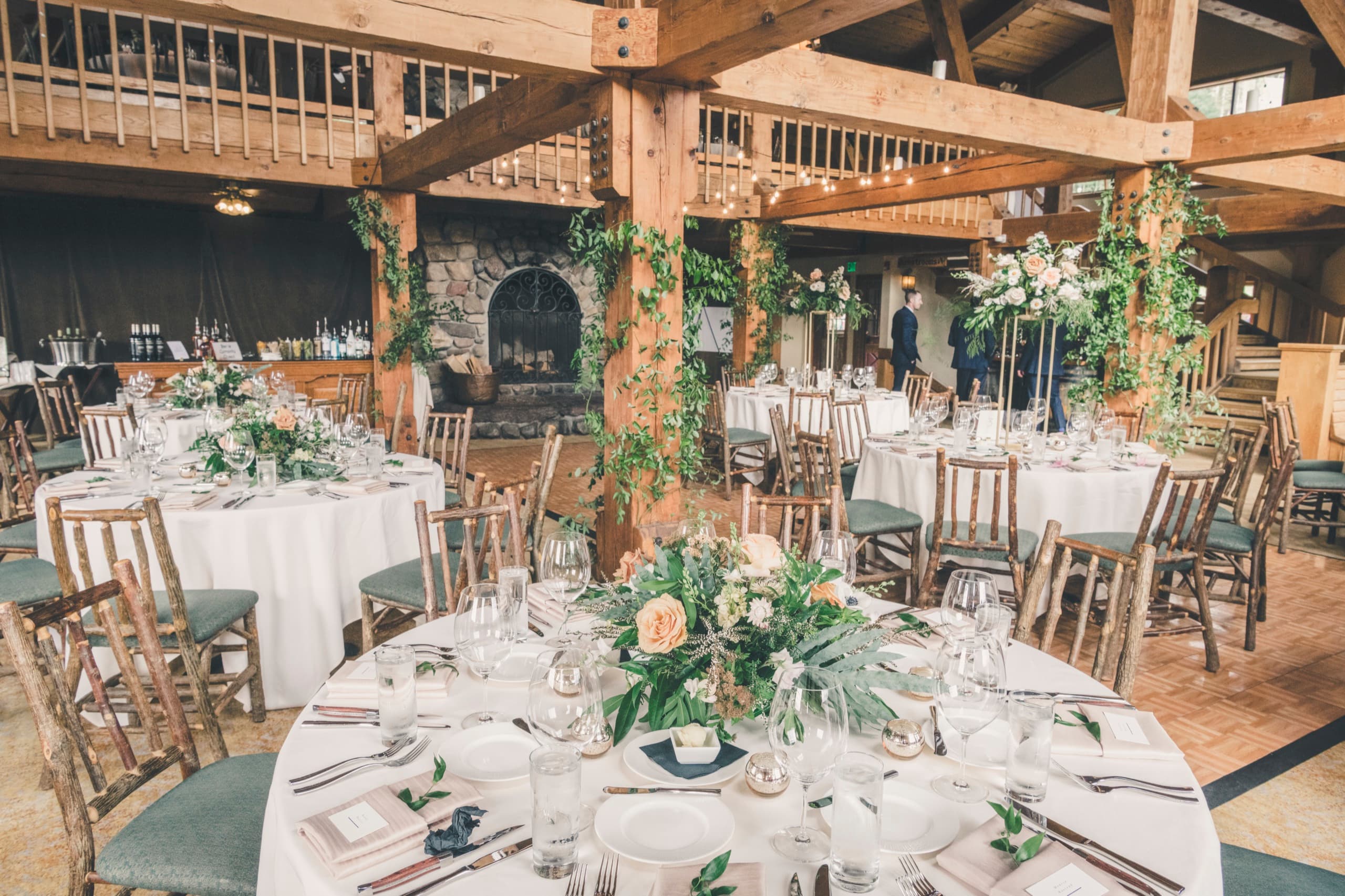 Gorrono Ranch lodge interior — timber beams, stone fireplace, round reception tables set with greenery