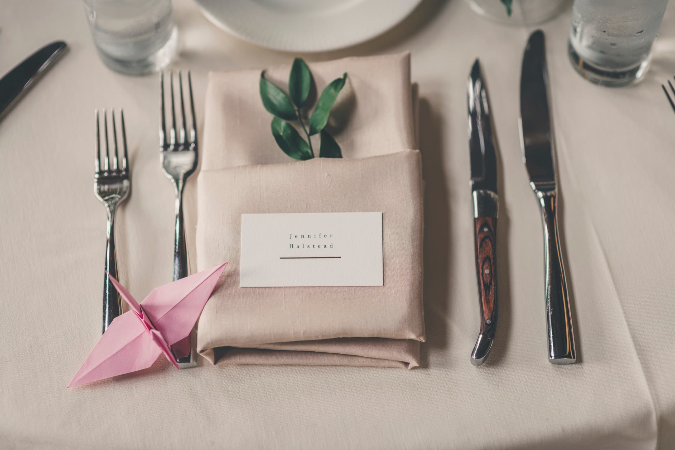Place setting detail at Meghan and Brent's reception — pink origami crane on linen napkin with name card