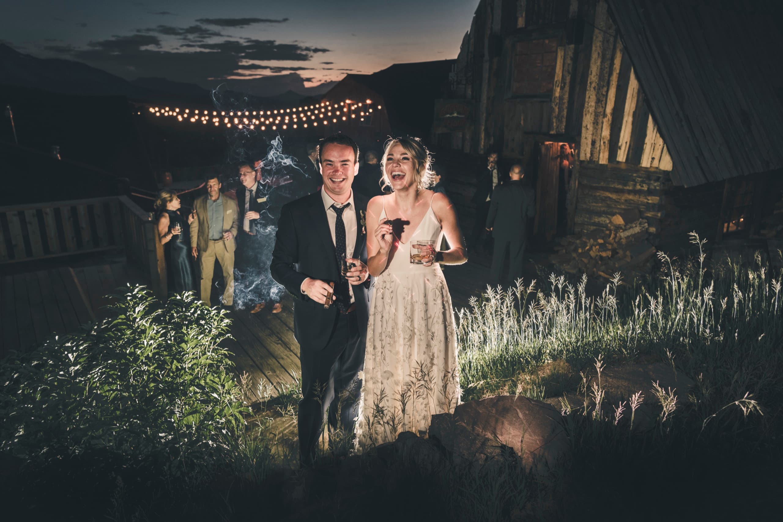 Meghan laughing wildly beside Brent holding a cigar under string lights at the Gorrono Ranch reception