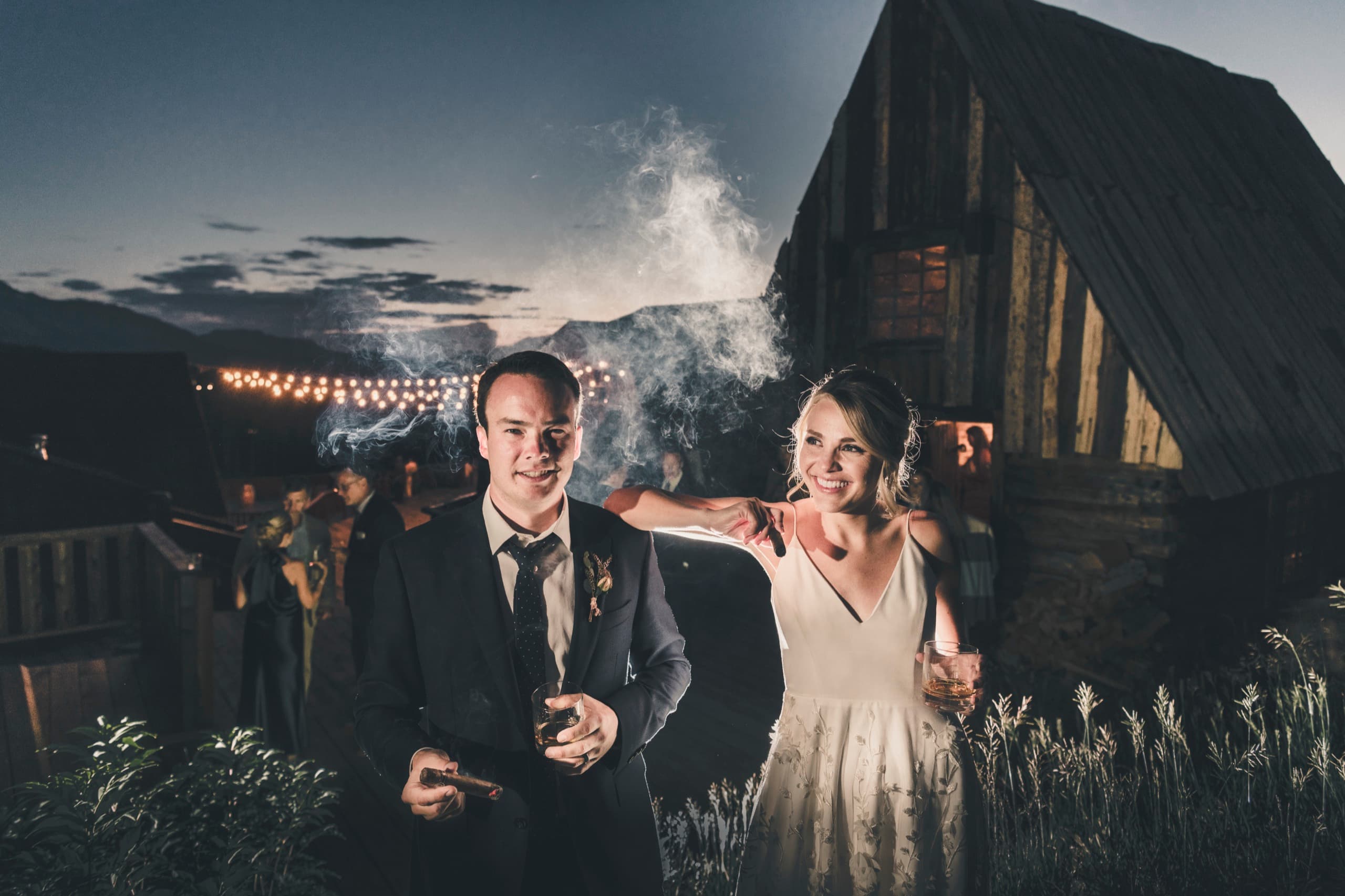 Meghan and Brent at blue hour with off-camera flash, Brent with cigar and whiskey, lodge silhouette behind