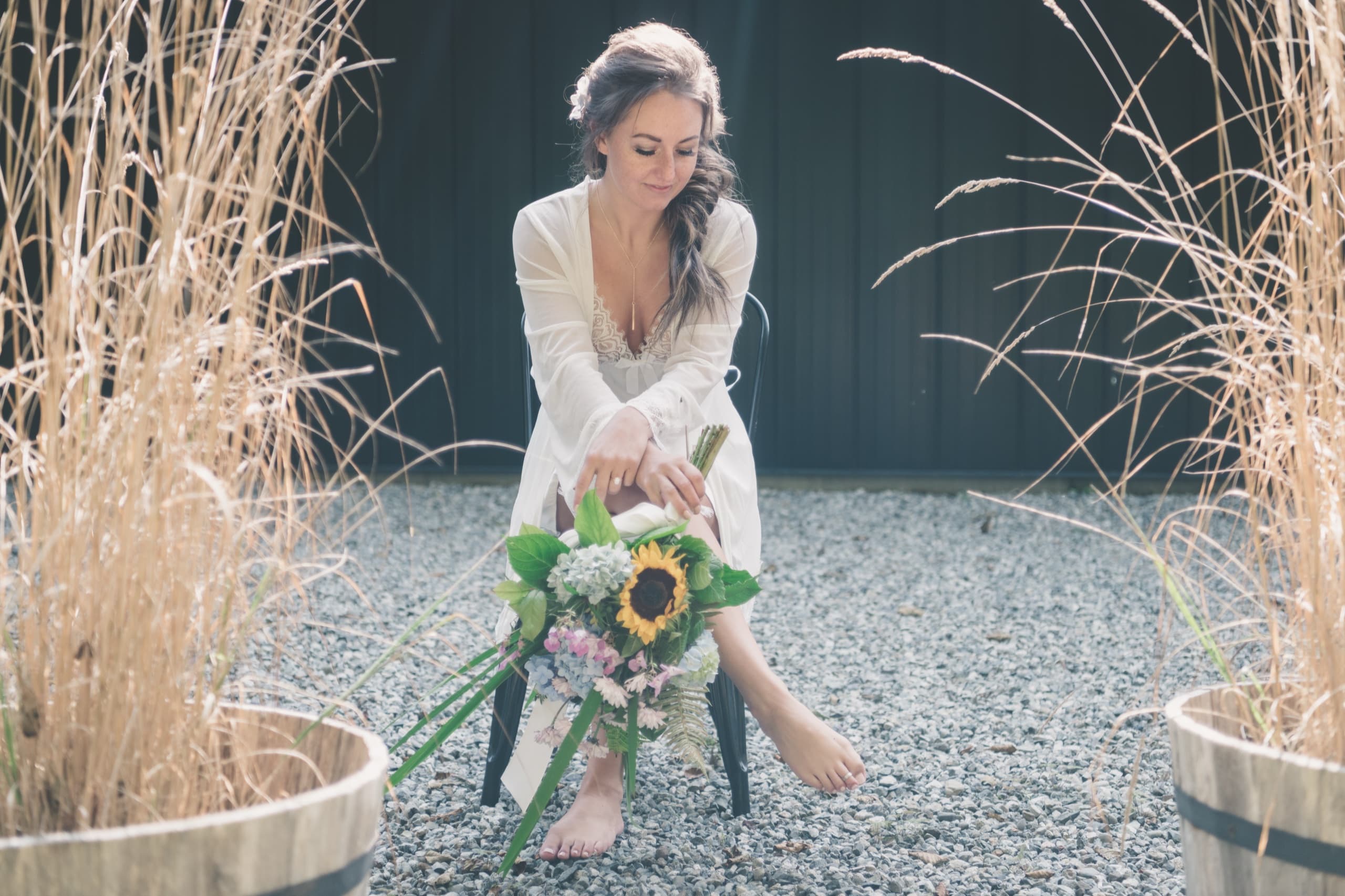 Rachel arranging her sunflower bouquet barefoot in the tall grass before the ceremony