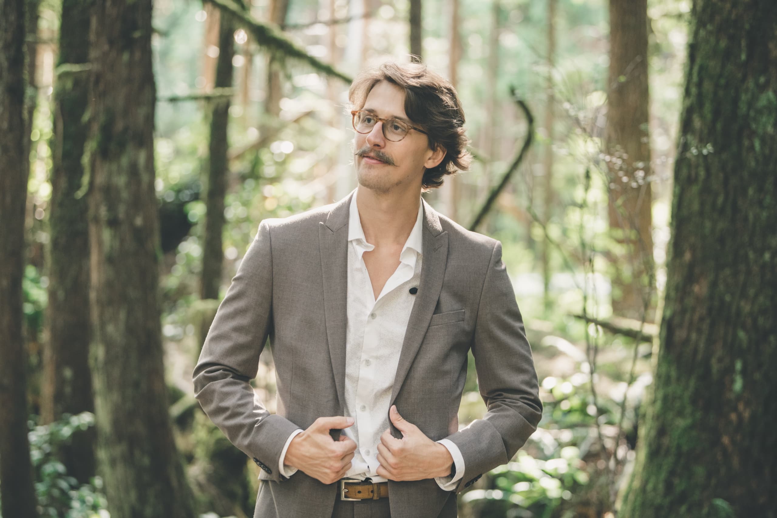Solo portrait of Peter in the Tofino rainforest, hands on his jacket lapels