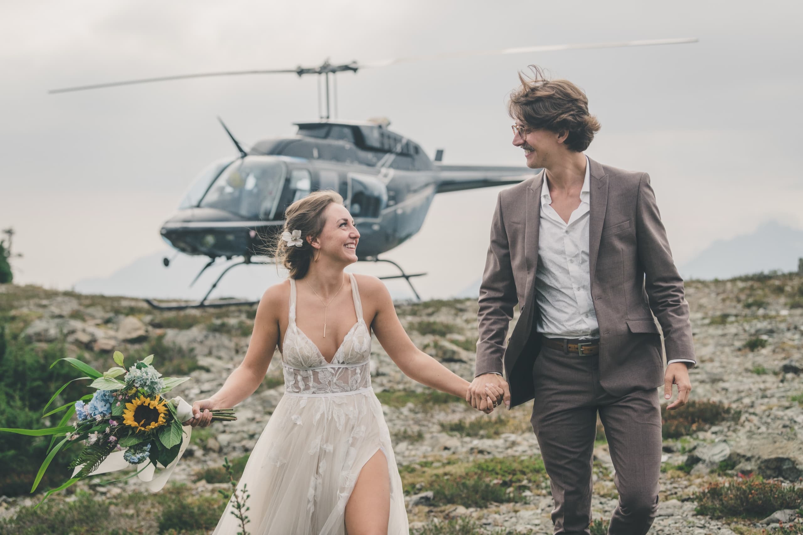 Rachel and Peter holding hands on the alpine tundra with the helicopter parked behind them