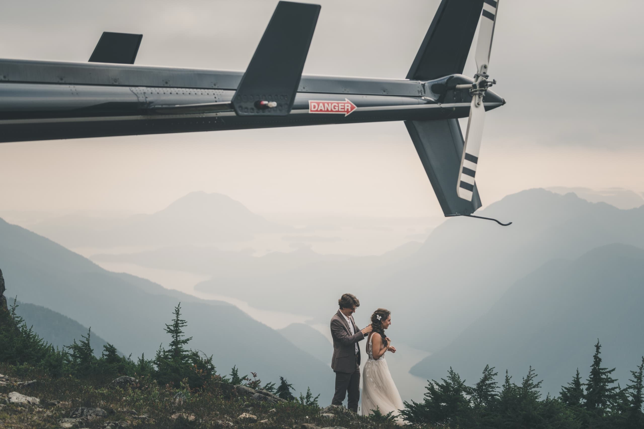 Cinematic wide of the helicopter tail looming over Rachel and Peter on a misty mountain ridge