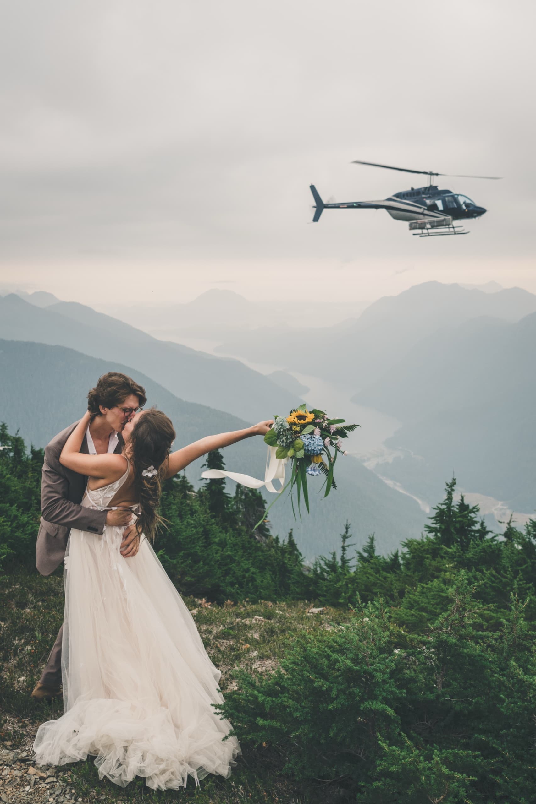 Rachel and Peter kissing as the helicopter hovers overhead above the Tofino mountain valley