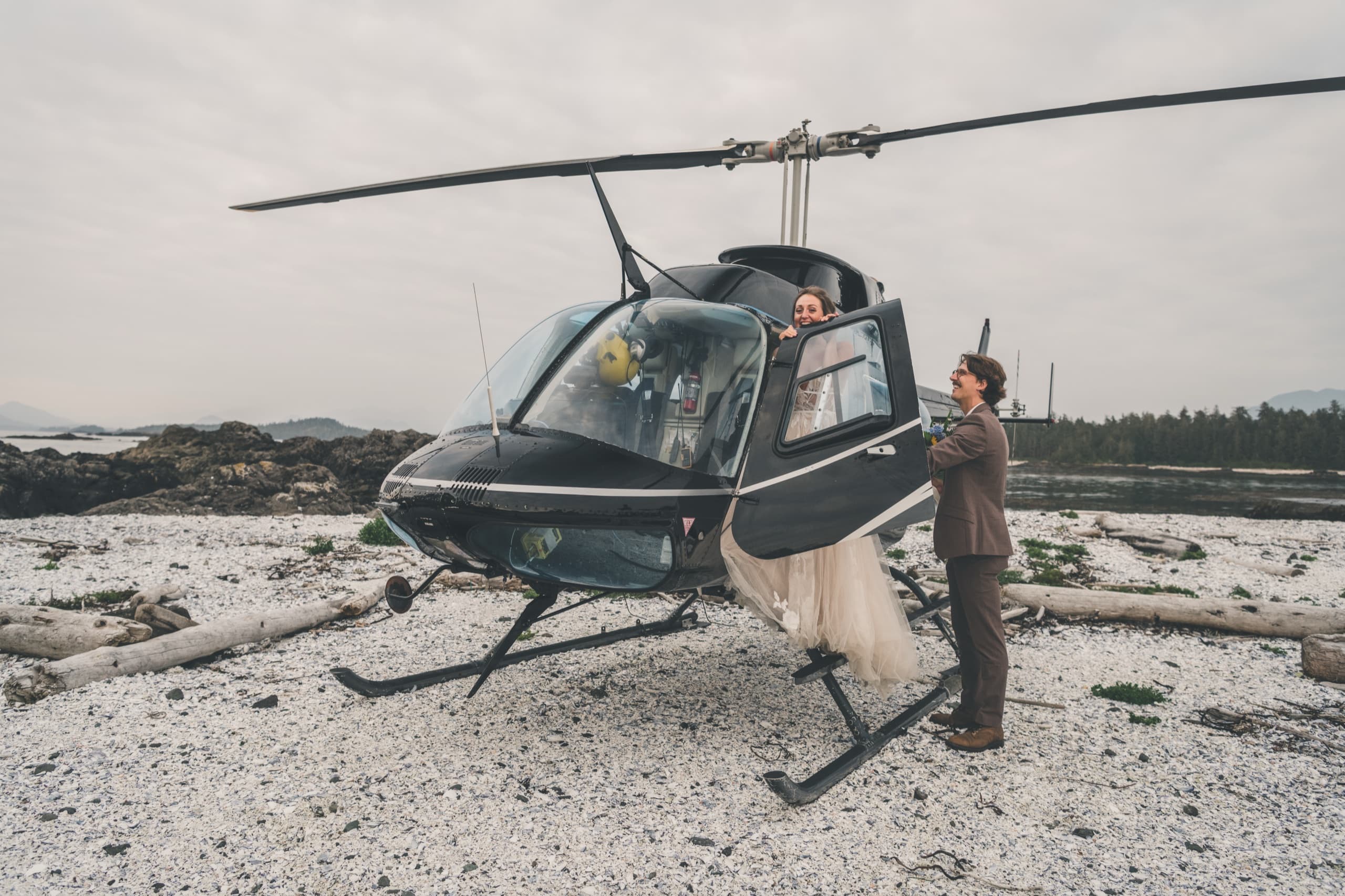 Rachel climbing into the helicopter on a remote pebble beach with Peter assisting