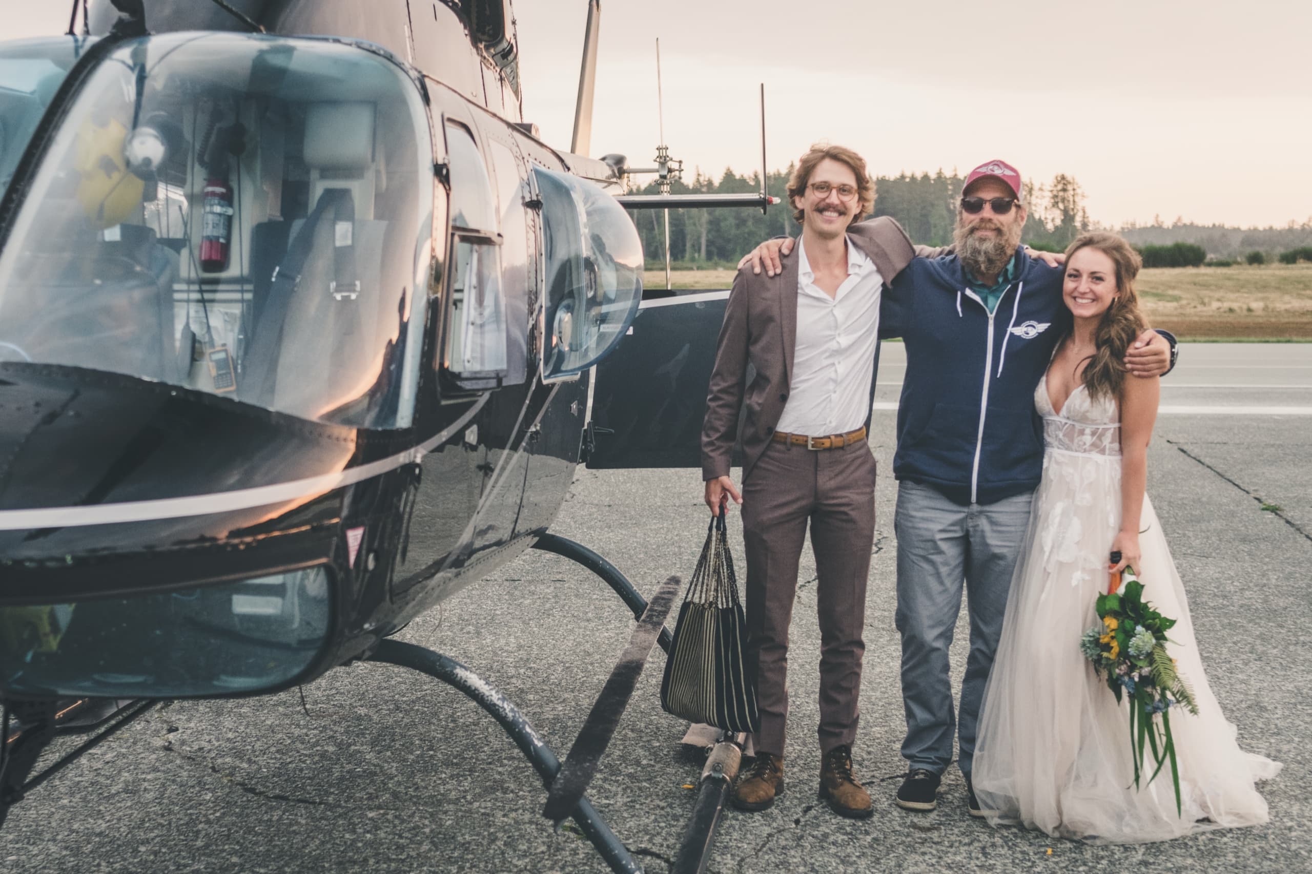 Rachel and Peter posing on the tarmac with their helicopter pilot, behind-the-scenes
