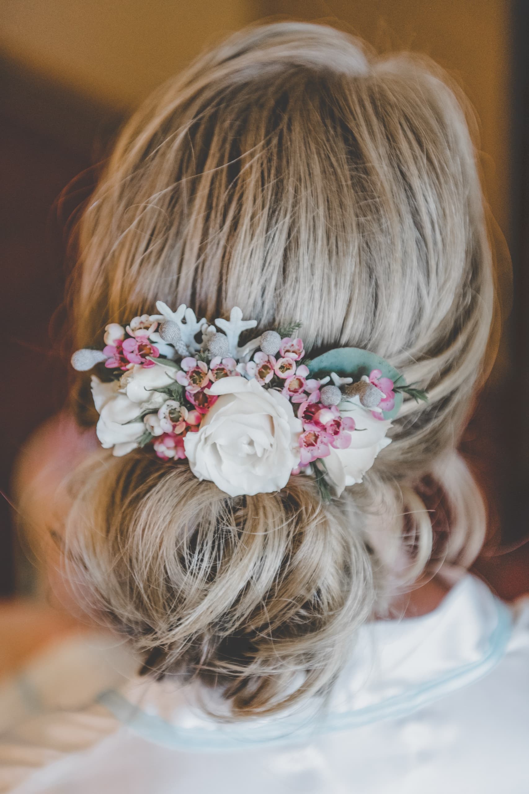 Detail of Jolly's low updo with floral hair piece — white roses and pink wax flower