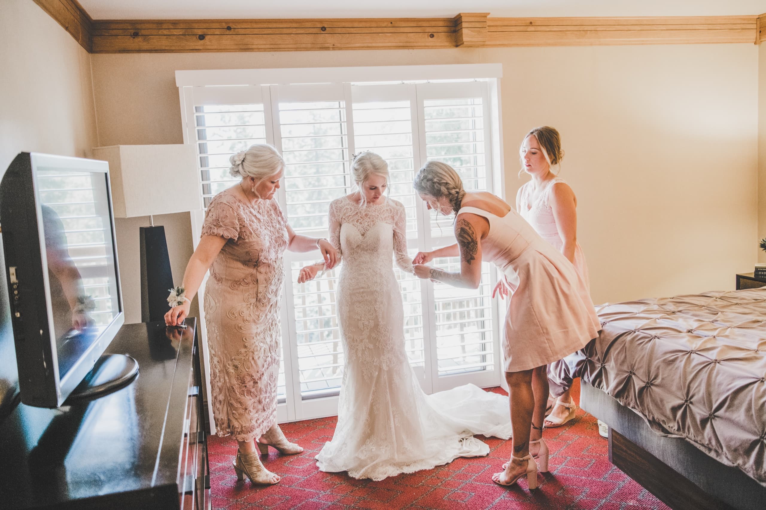 Jolly with her mother and bridesmaids helping her into her lace dress in the Tenaya Lodge suite