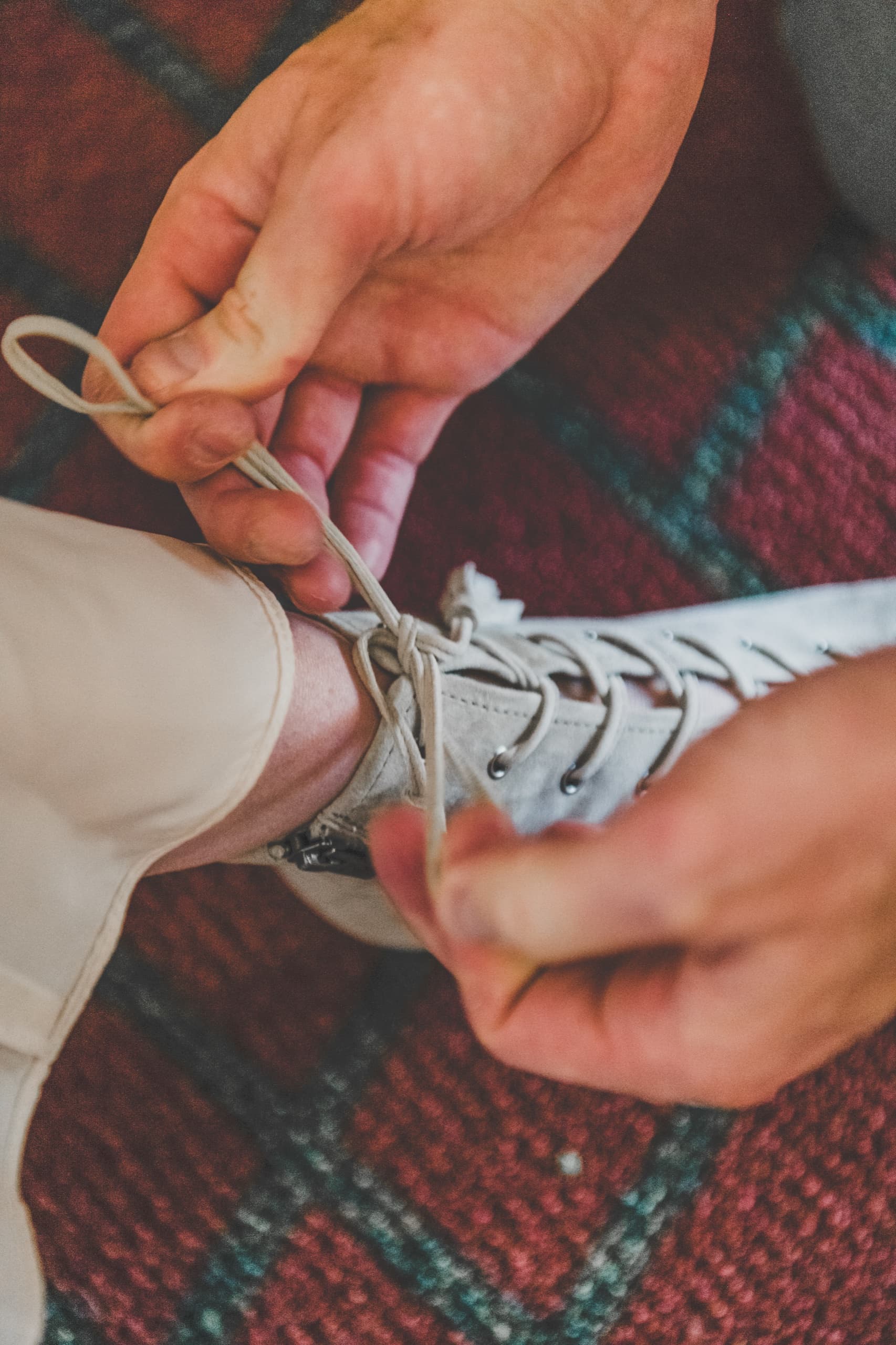 Billy lacing his white wedding boot on the patterned rug in the prep suite, getting-ready detail