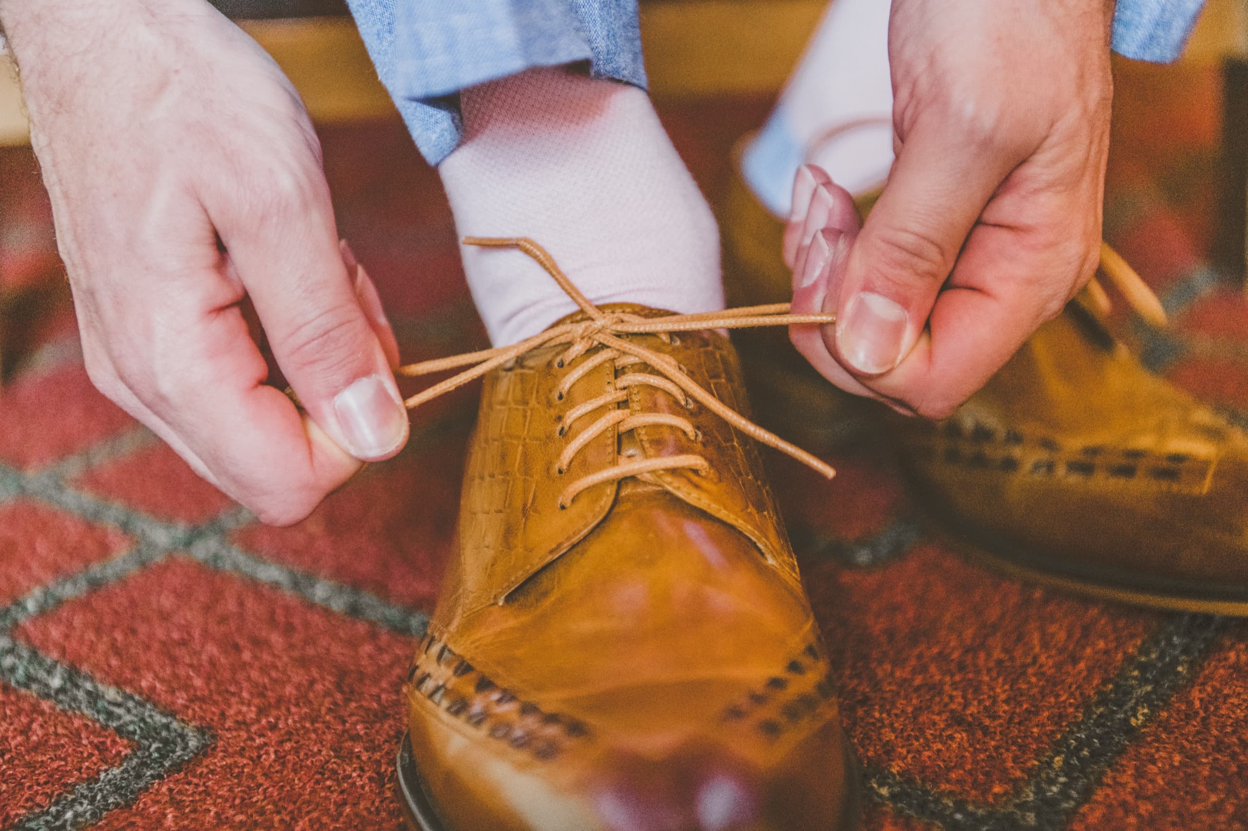 Billy tying his brown leather oxford on the red patterned carpet of the Tenaya prep suite