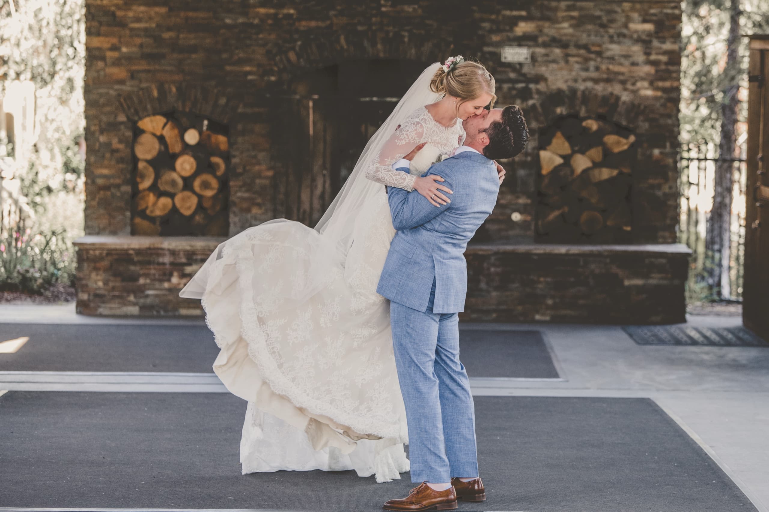 Billy lifts Jolly in a joyful embrace at the Tenaya Lodge stone fireplace patio, dress flowing
