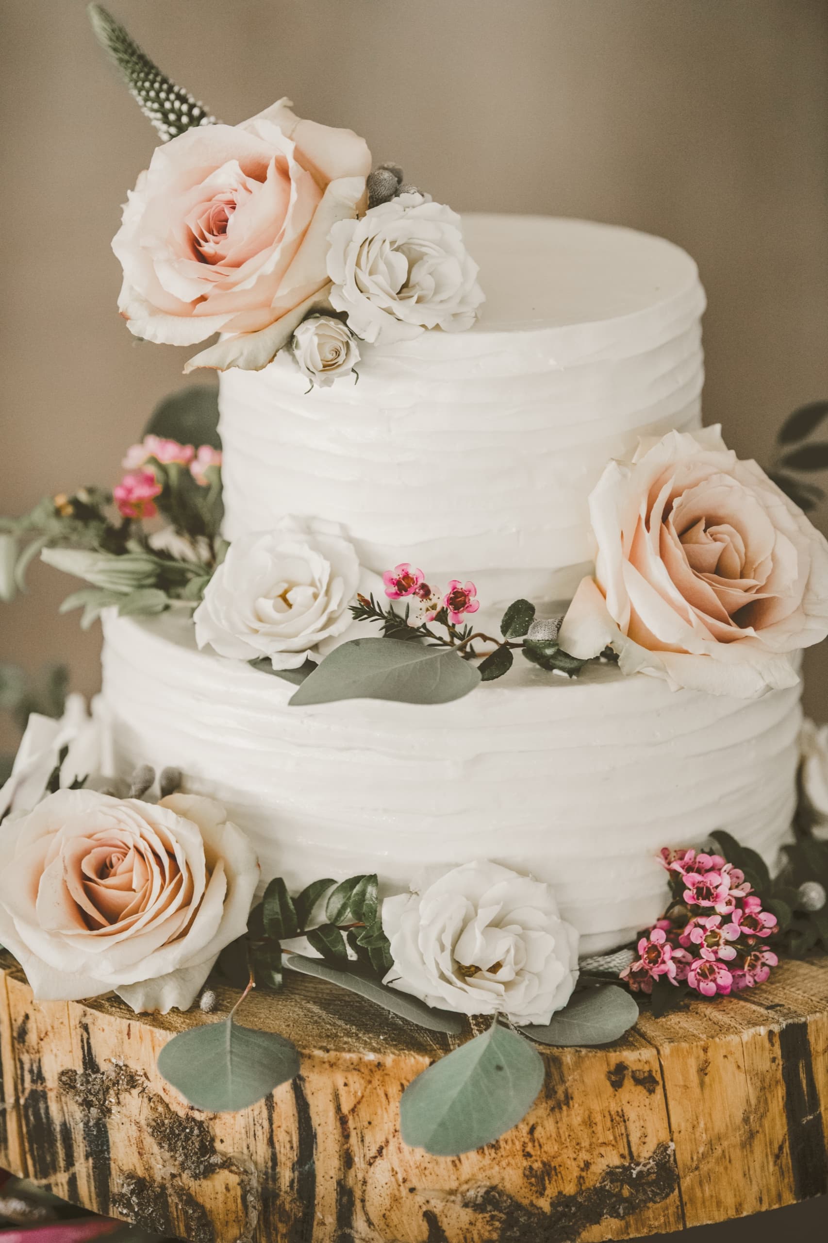 Jolly and Billy's two-tier white wedding cake with blush roses on a wood slab in soft natural light